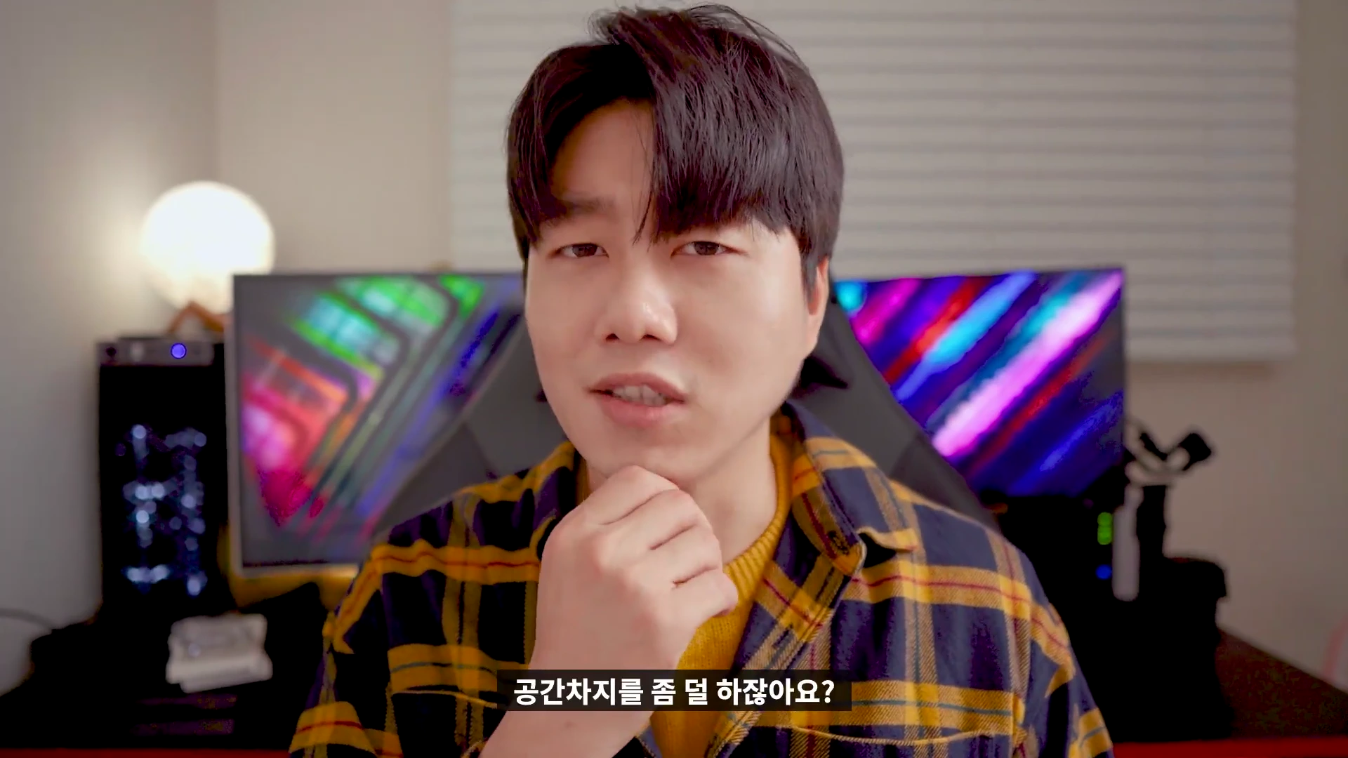 체크무늬 셔츠를 입고 턱에 손을 댄 채 정면을 바라보는 남성