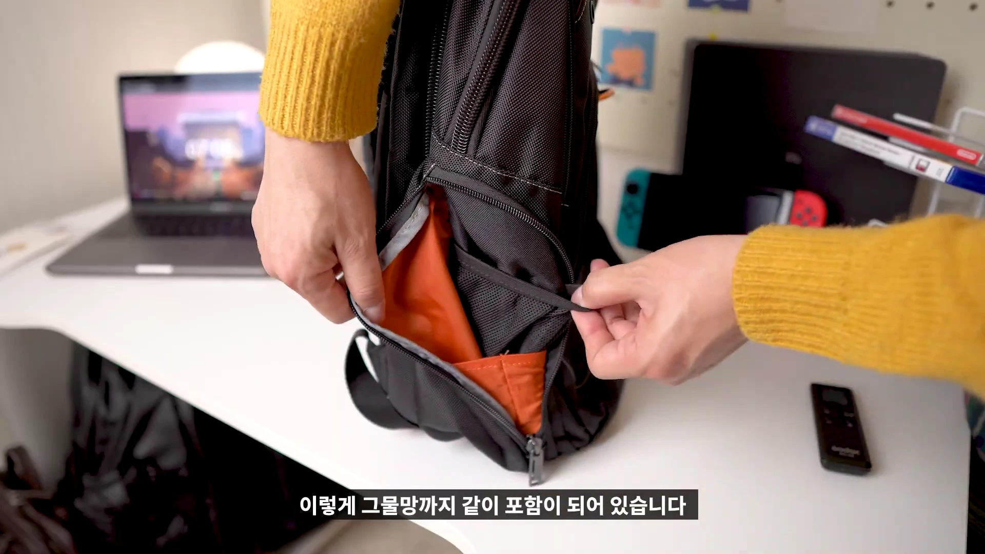 노란색 니트를 입은 사람이 검은색 백팩의 측면 수납 포켓을 열어 내부의 그물망을 보여주고 있다.