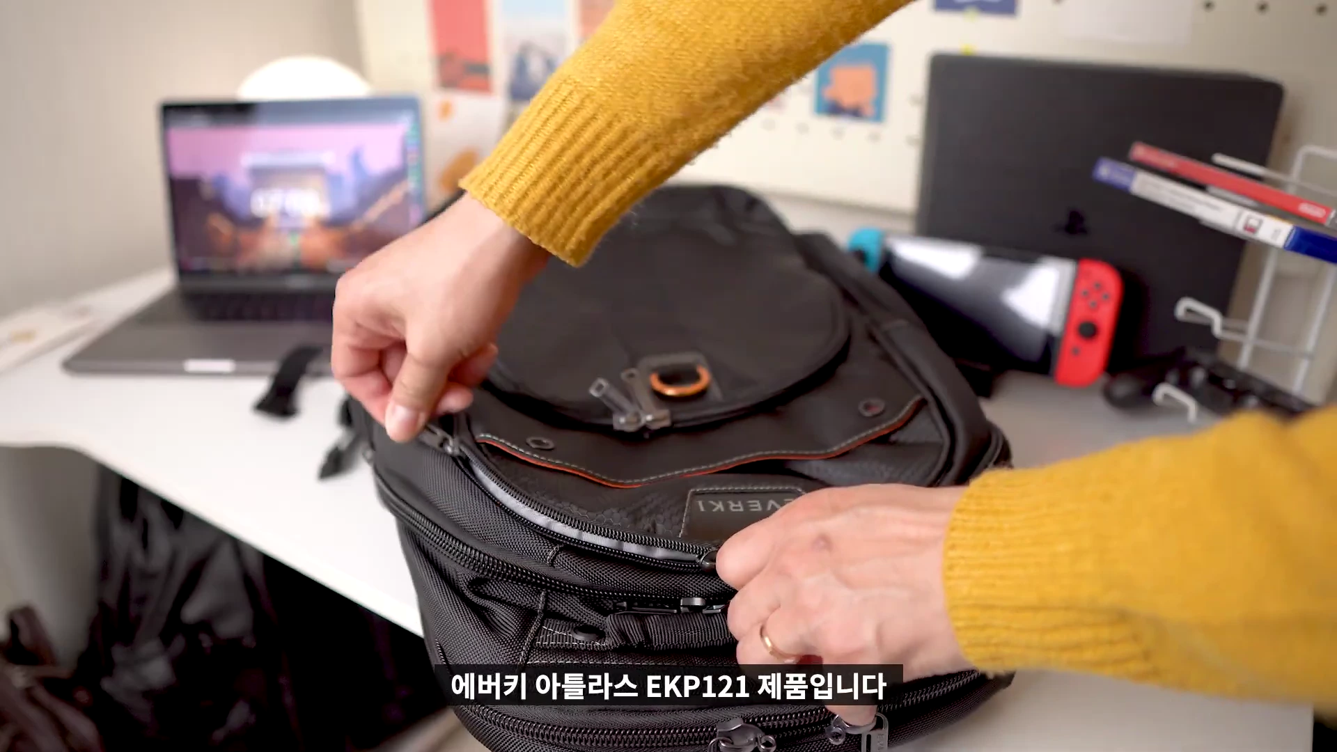 노란색 니트를 입은 사람이 책상 위에서 검은색 백팩의 지퍼를 열고 있는 모습