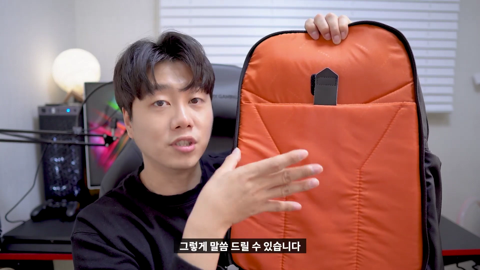 실내에서 한 남성이 주황색 안감이 돋보이는 비즈니스 백팩의 내부 수납공간을 손으로 가리키며 설명하고 있다.