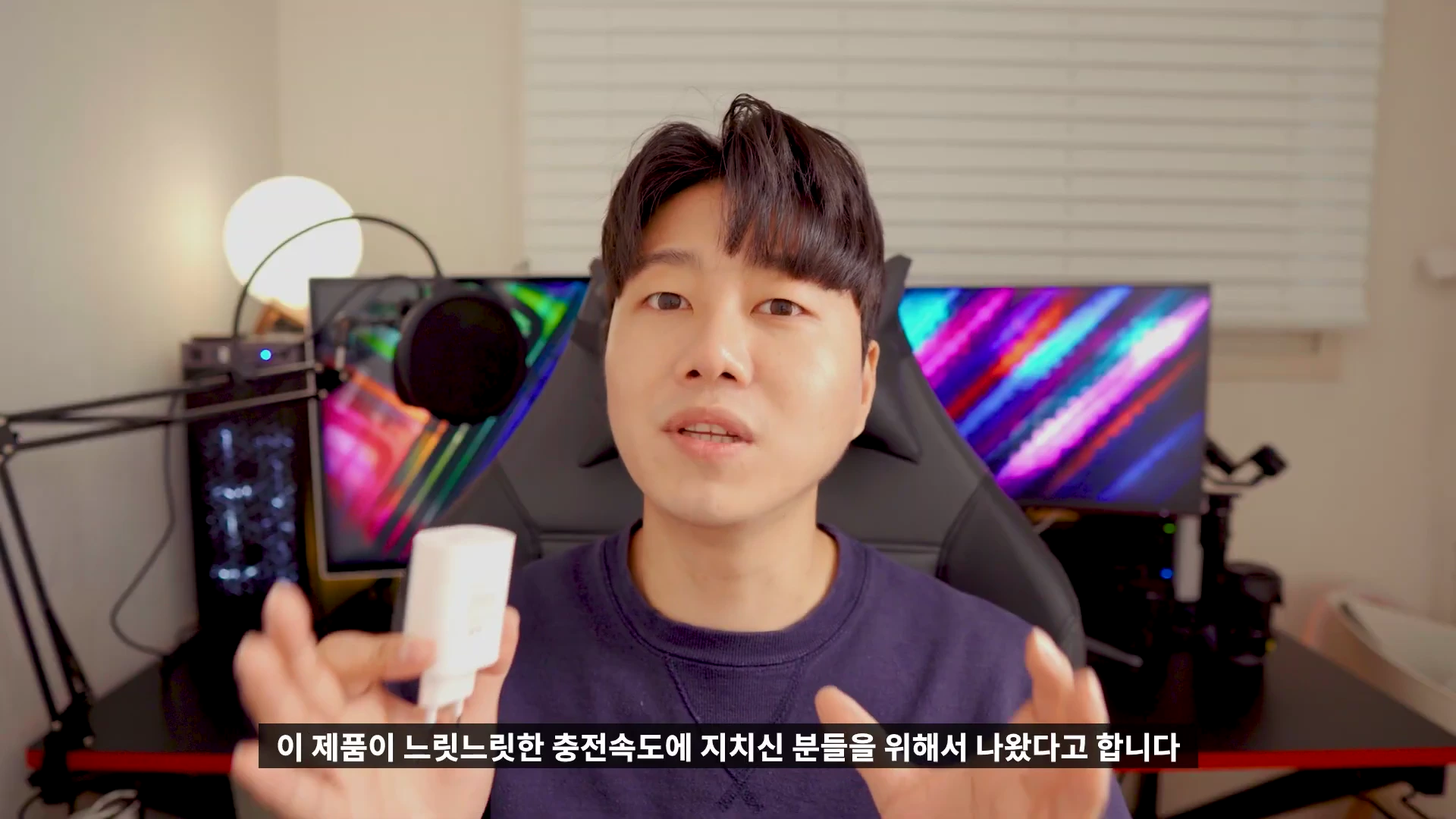 책상 앞에 앉아 흰색 충전 어댑터를 손에 들고 설명하는 남성
