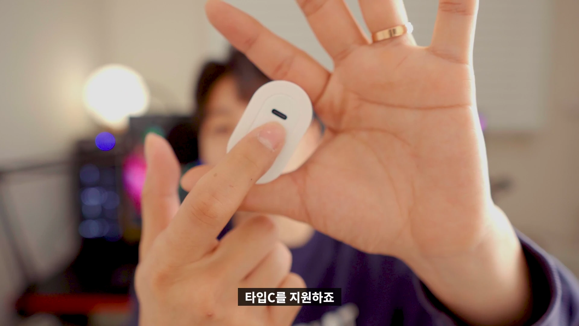 한 사람이 손바닥 위에 작고 흰색의 타원형 충전 어댑터를 올려두고 손가락으로 가리키고 있다.