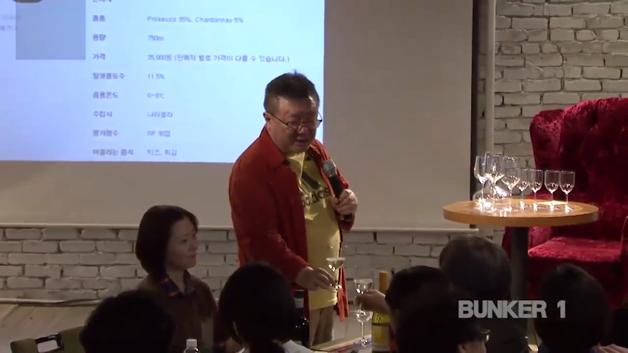 강연자가 와인 잔을 들고 청중과 건배하는 모습이 담긴 실내 강연 현장