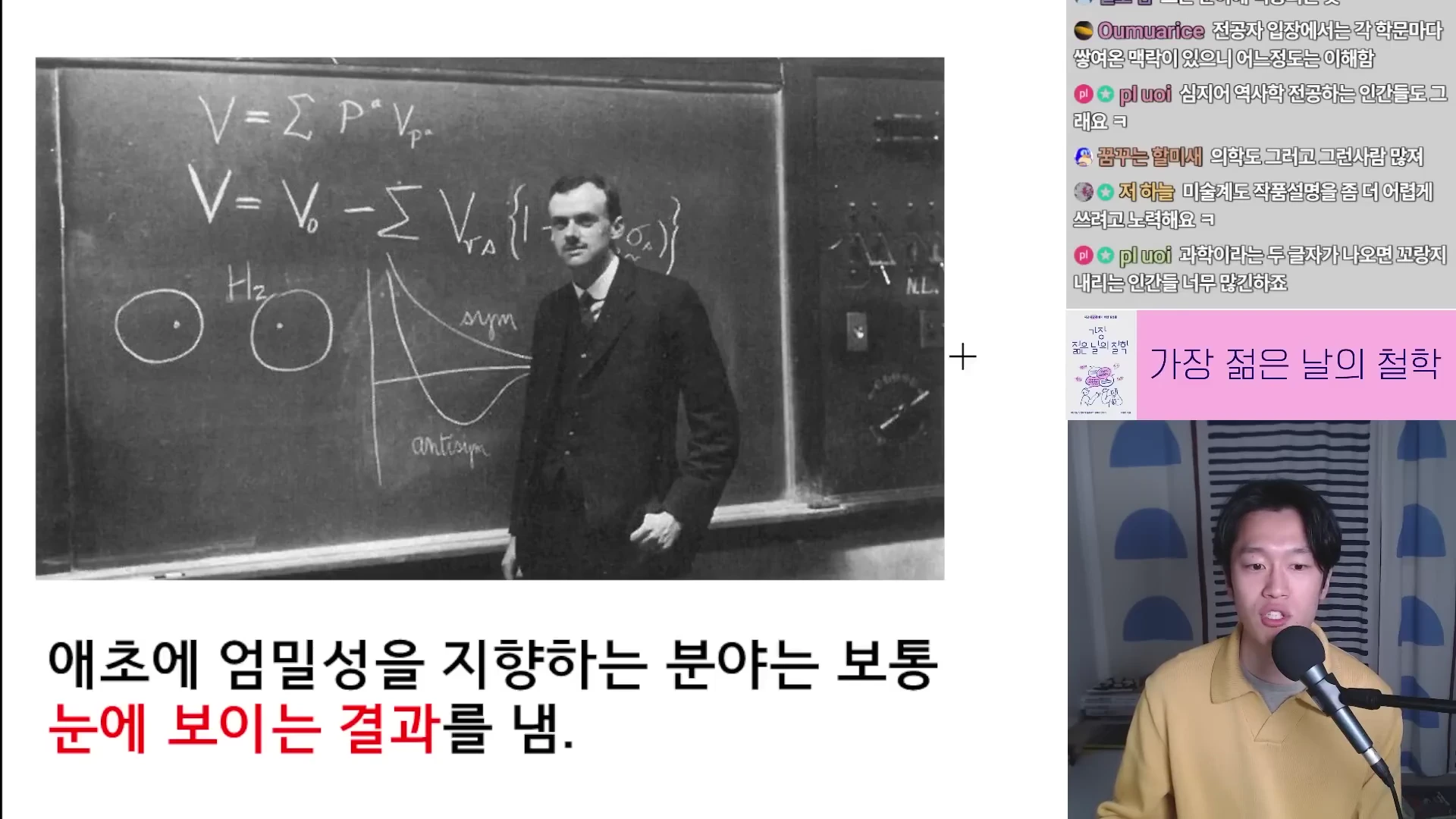 복잡한 수식이 적힌 칠판 앞에 서 있는 물리학자와 그 옆에 마이크를 잡고 말하는 남성이 보이는 영상 화면