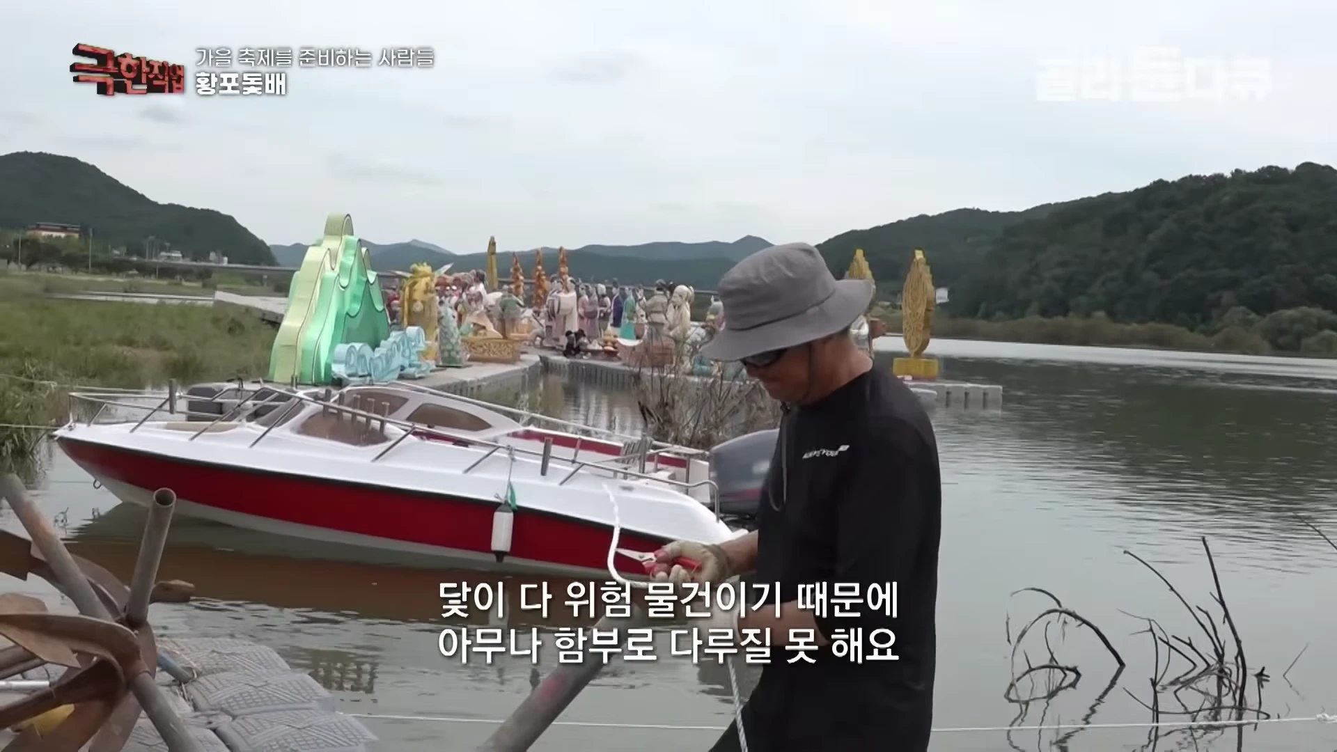 강가에서 모자를 쓴 작업자가 로프를 다루며 작업 중인 모습과 인근에 정박된 보트들