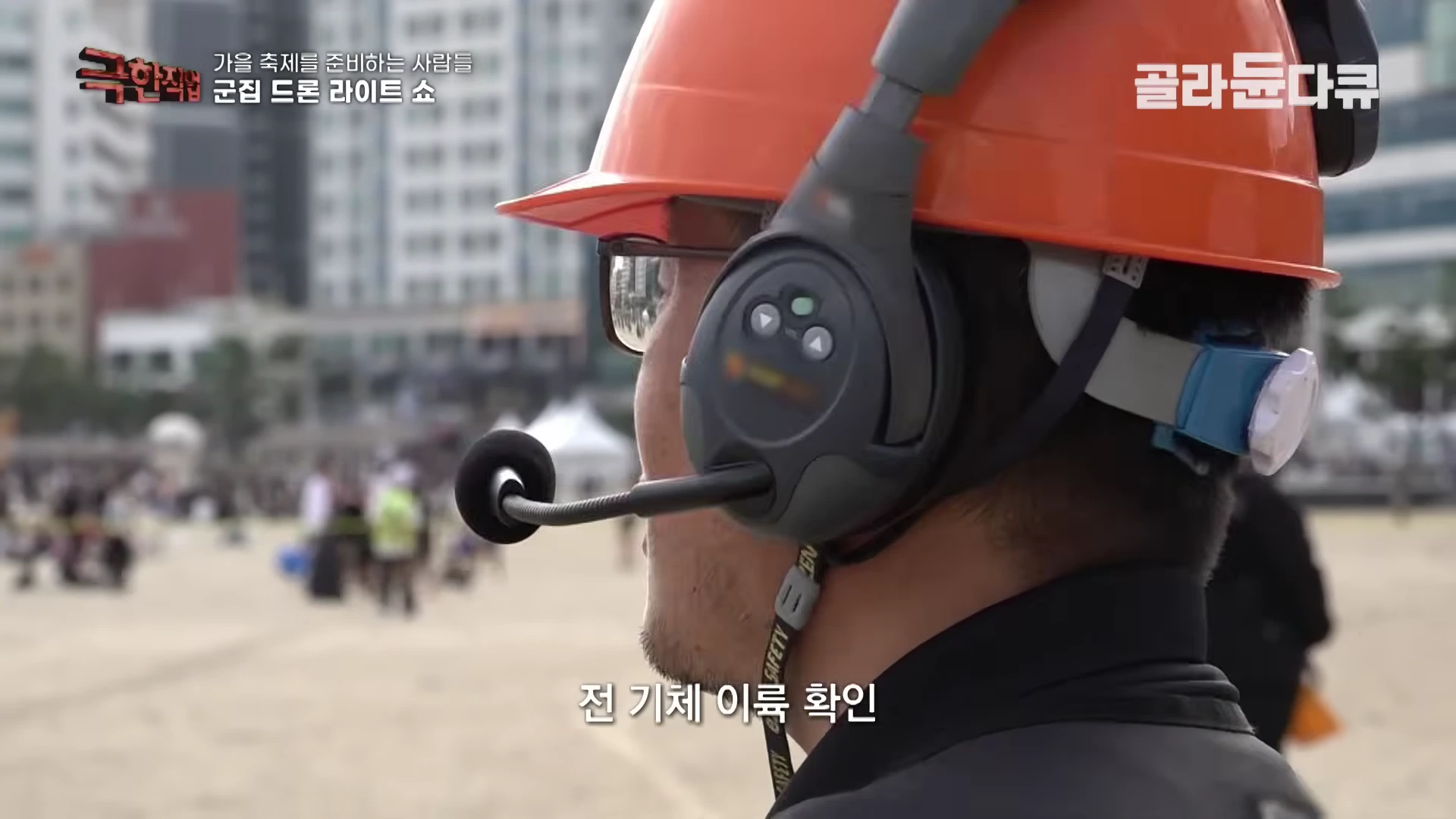 주황색 안전모와 헤드셋을 착용한 현장 관계자가 무언가를 응시하며 통신하고 있다.