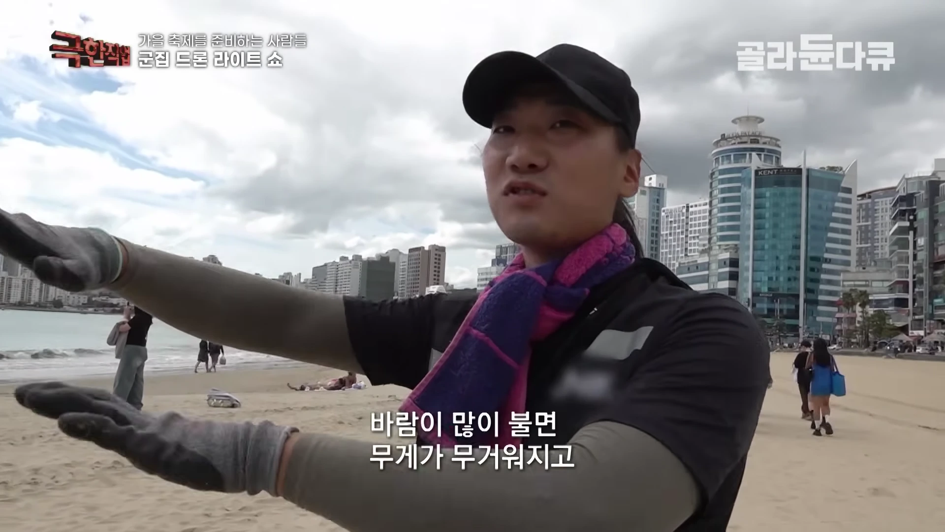 야외 해변에서 검은 모자와 운동복 차림의 남성이 드론 쇼 준비 과정에 대해 설명하며 손짓을 하고 있다.