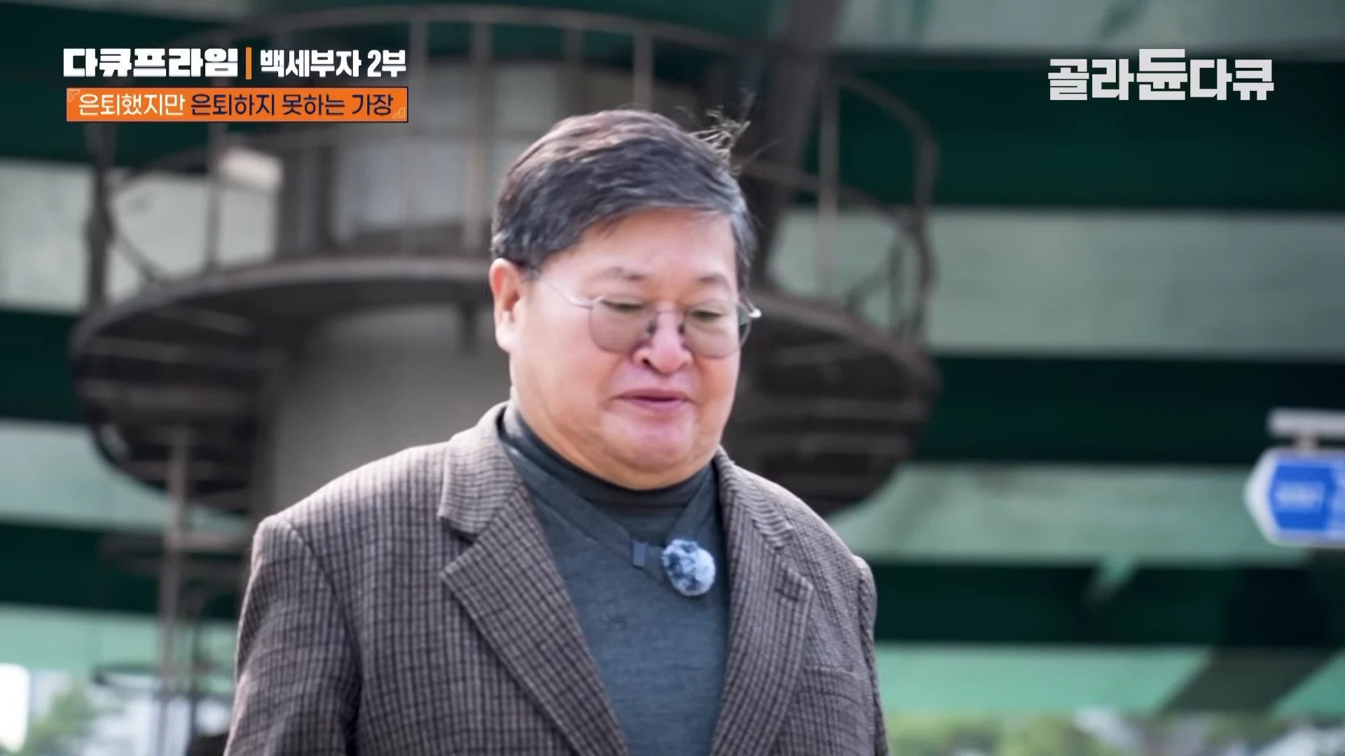 안경을 쓴 중년 남성이 무거운 표정으로 고개를 숙인 채 걷고 있는 모습
