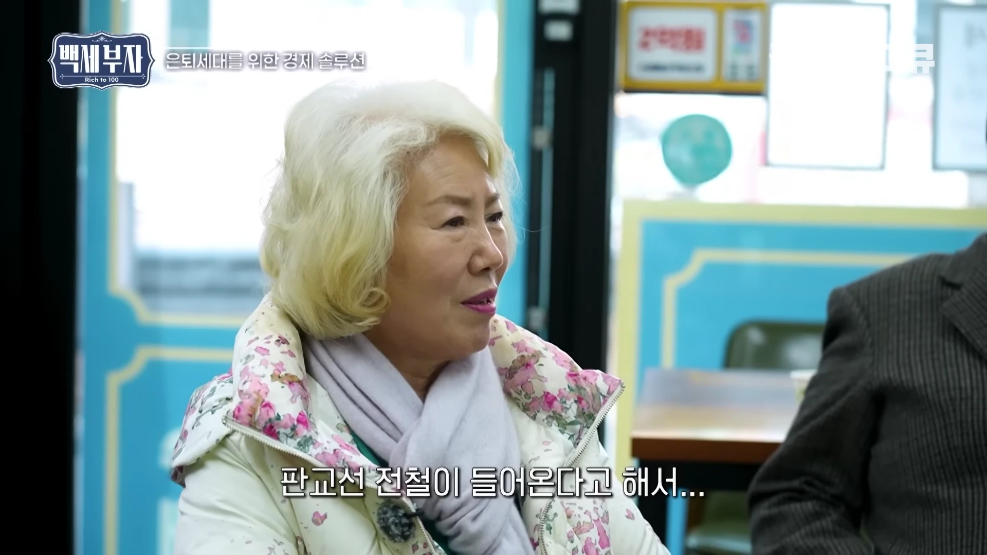 흰 머리의 중년 여성이 부동산 중개업소에 앉아 상담을 받고 있는 모습