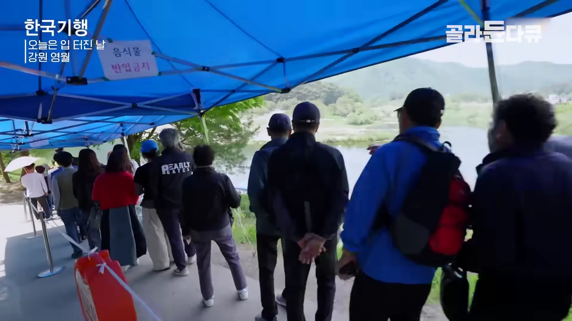푸른 천막 아래에서 사람들이 줄을 서서 대기하고 있는 모습.