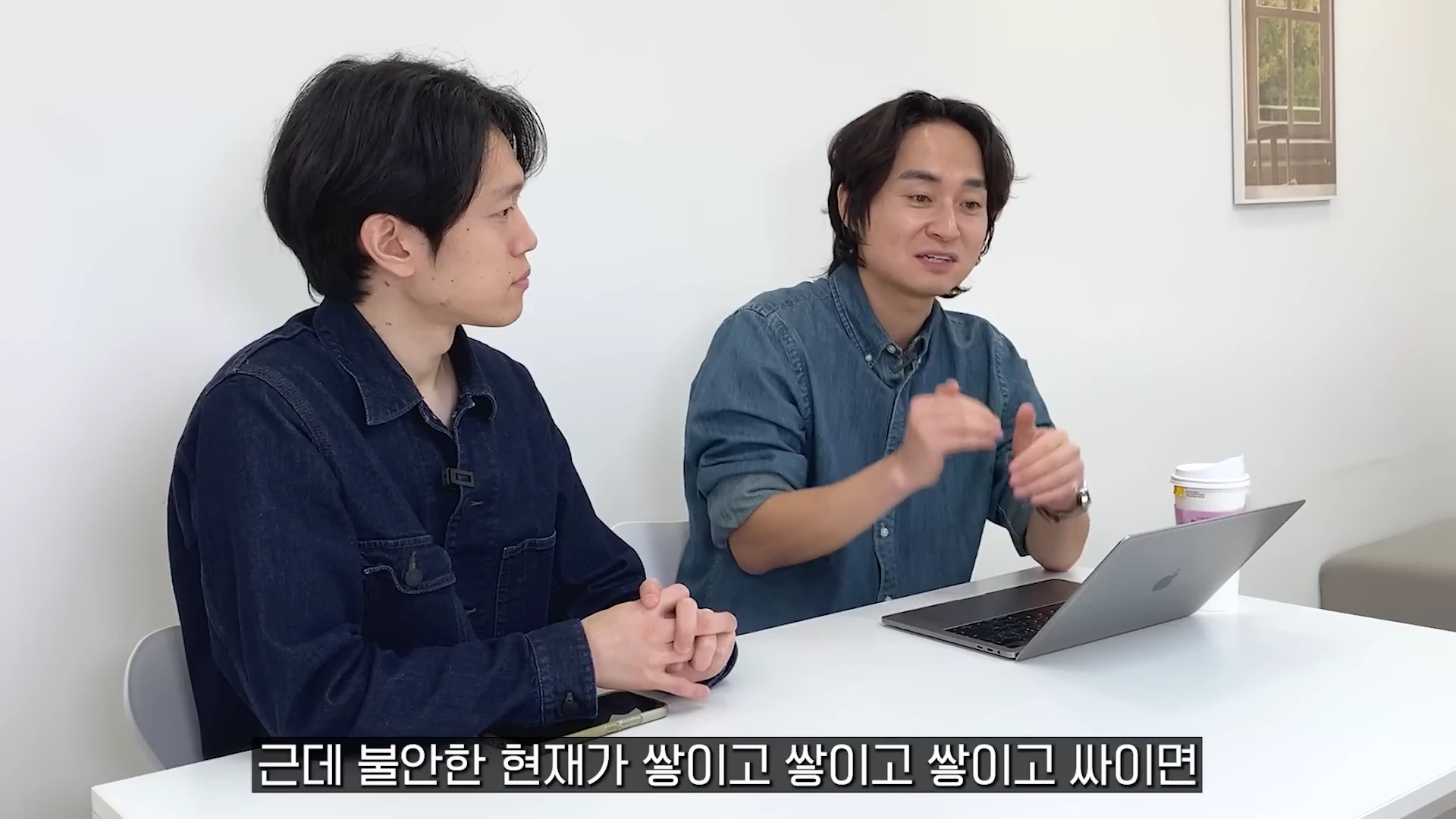 하얀 벽을 배경으로 테이블에 앉아 대화를 나누는 두 남성