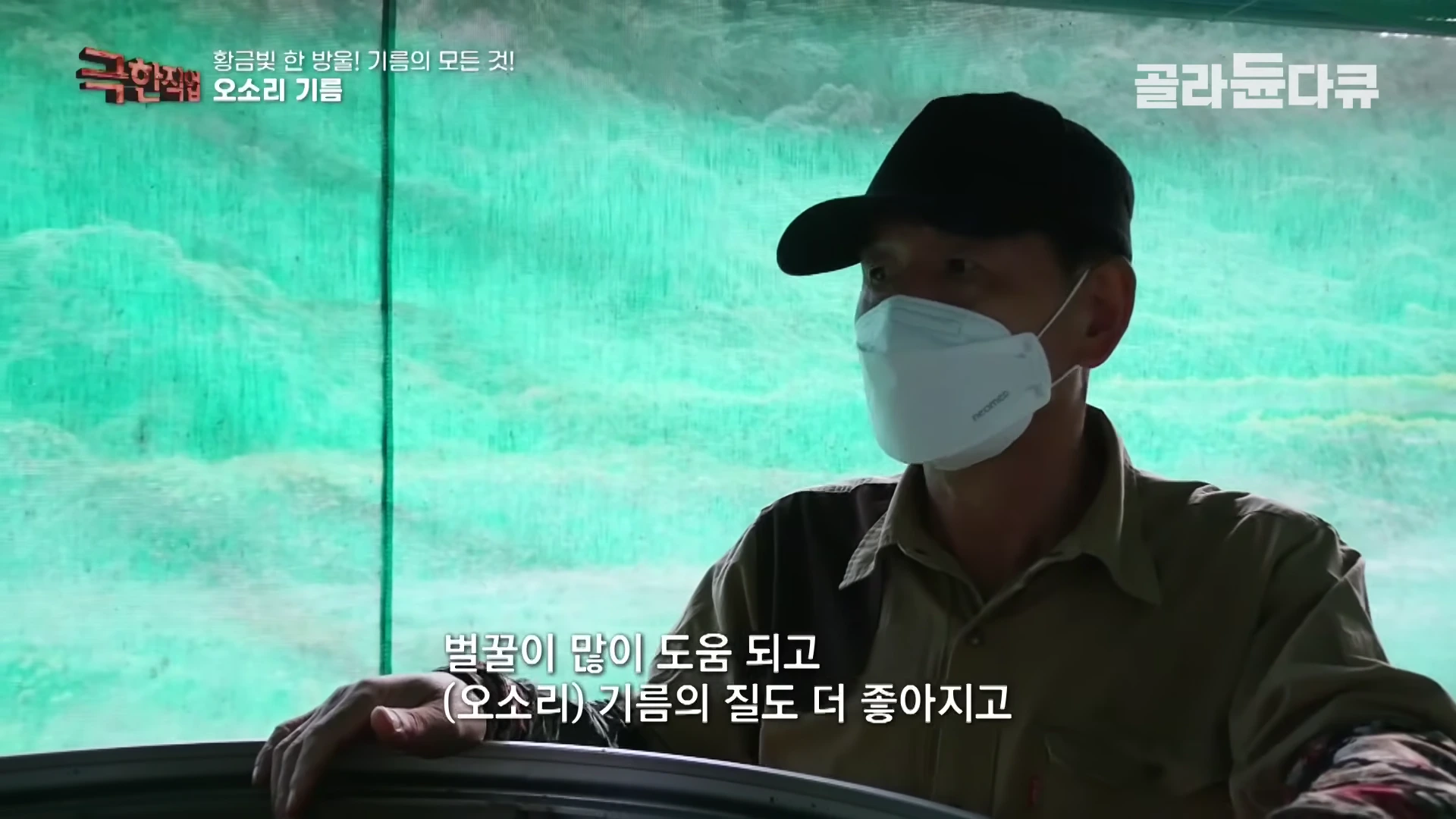 검은 모자와 흰색 마스크를 착용한 농장 관계자가 작업 설비 옆에 서서 인터뷰를 하고 있다.