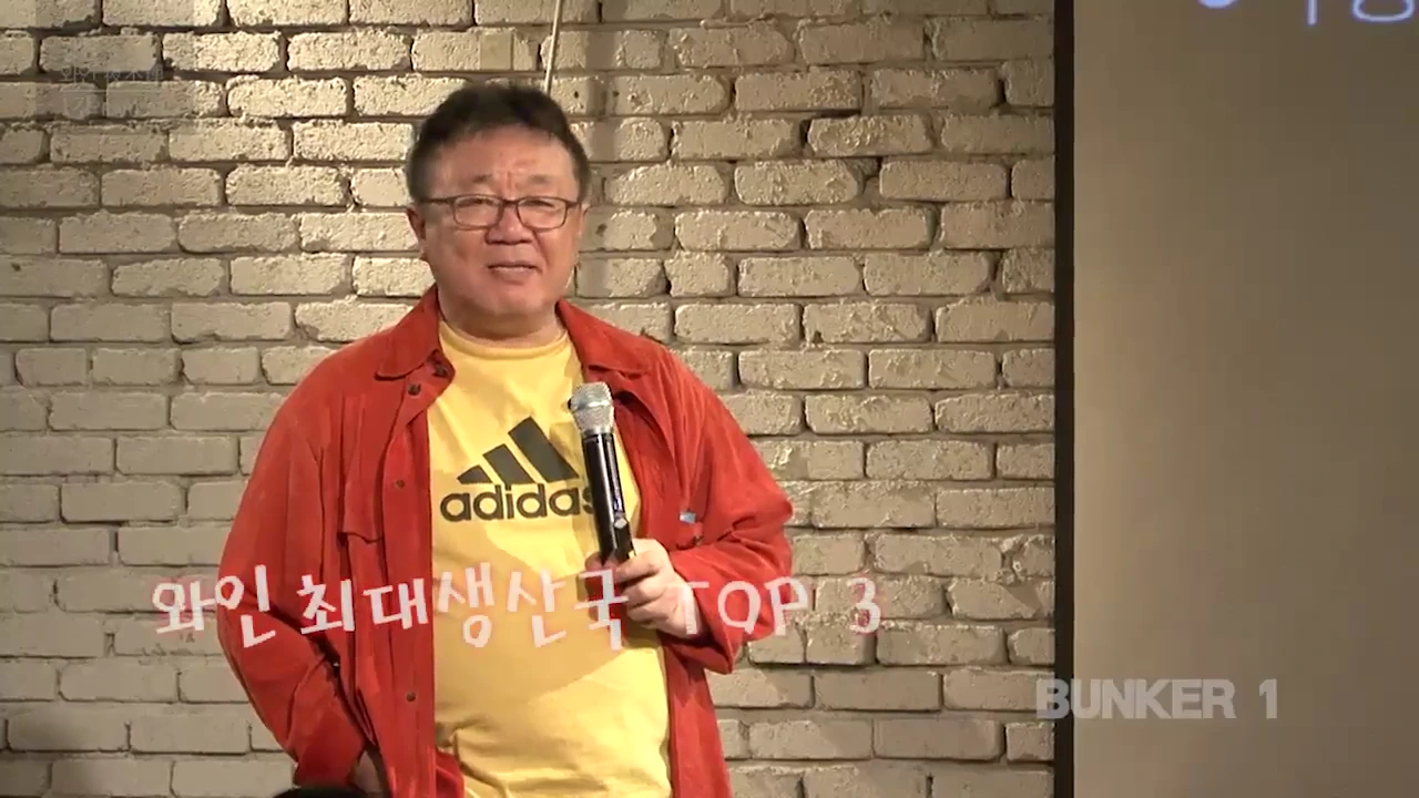 노란 티셔츠와 붉은 셔츠를 입은 중년 남성이 마이크를 잡고 강연하고 있다.