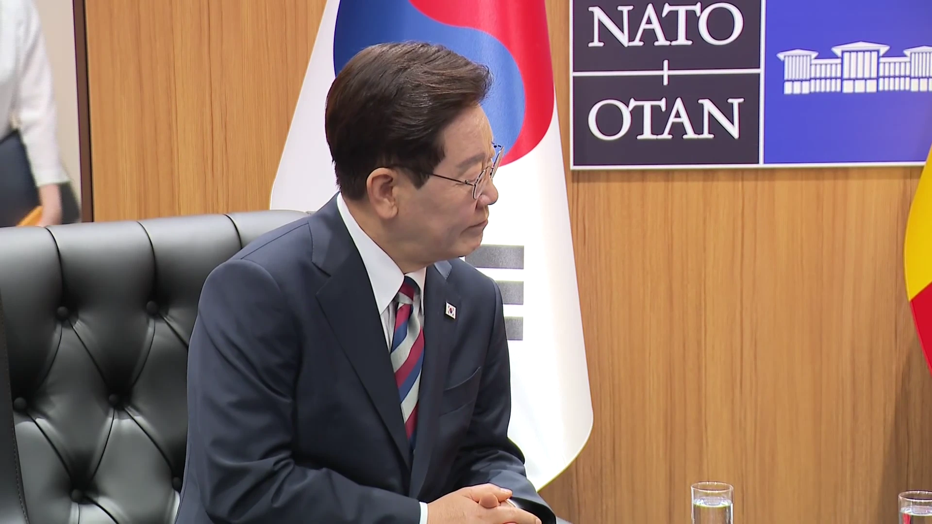 정장을 입은 남성이 태극기와 NATO 로고가 놓인 실내에서 회담에 집중하고 있는 모습