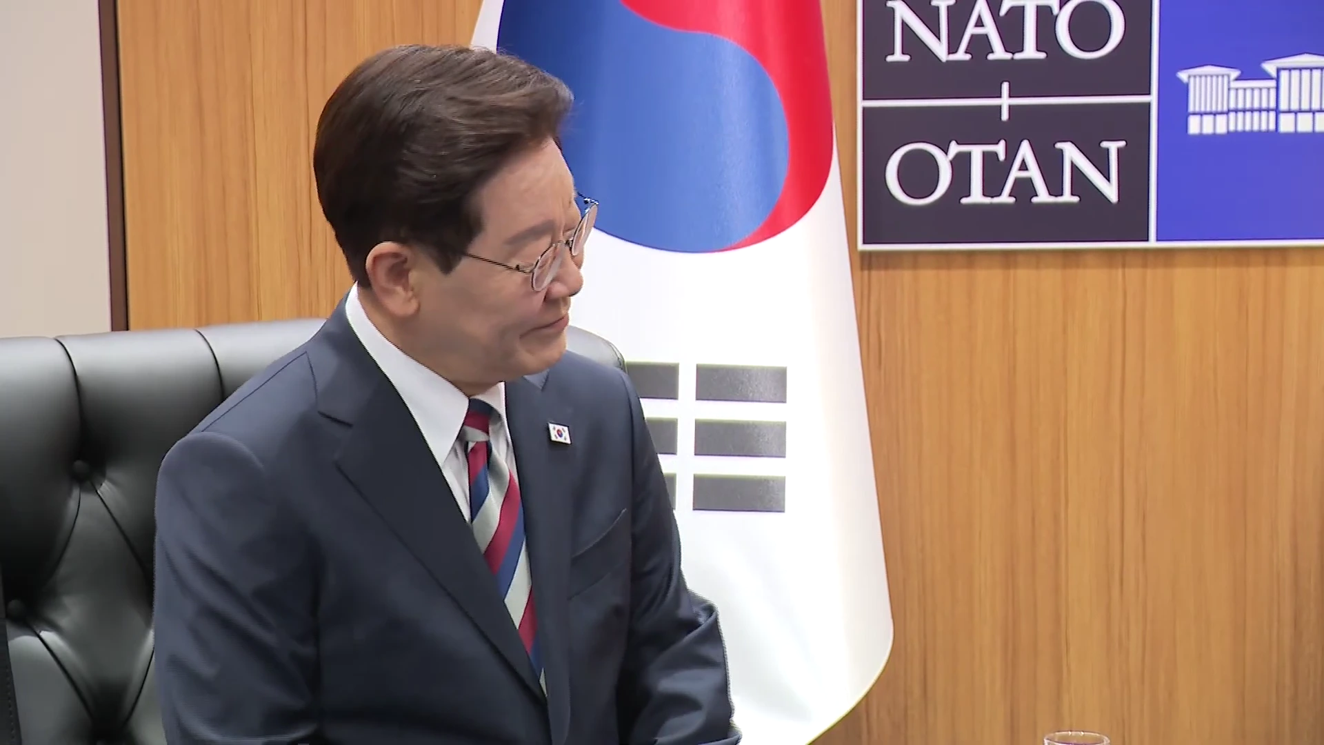 태극기와 NATO 로고가 벽면에 걸린 회의실에서 정장을 입은 한 남성이 앉아 대화를 나누는 모습