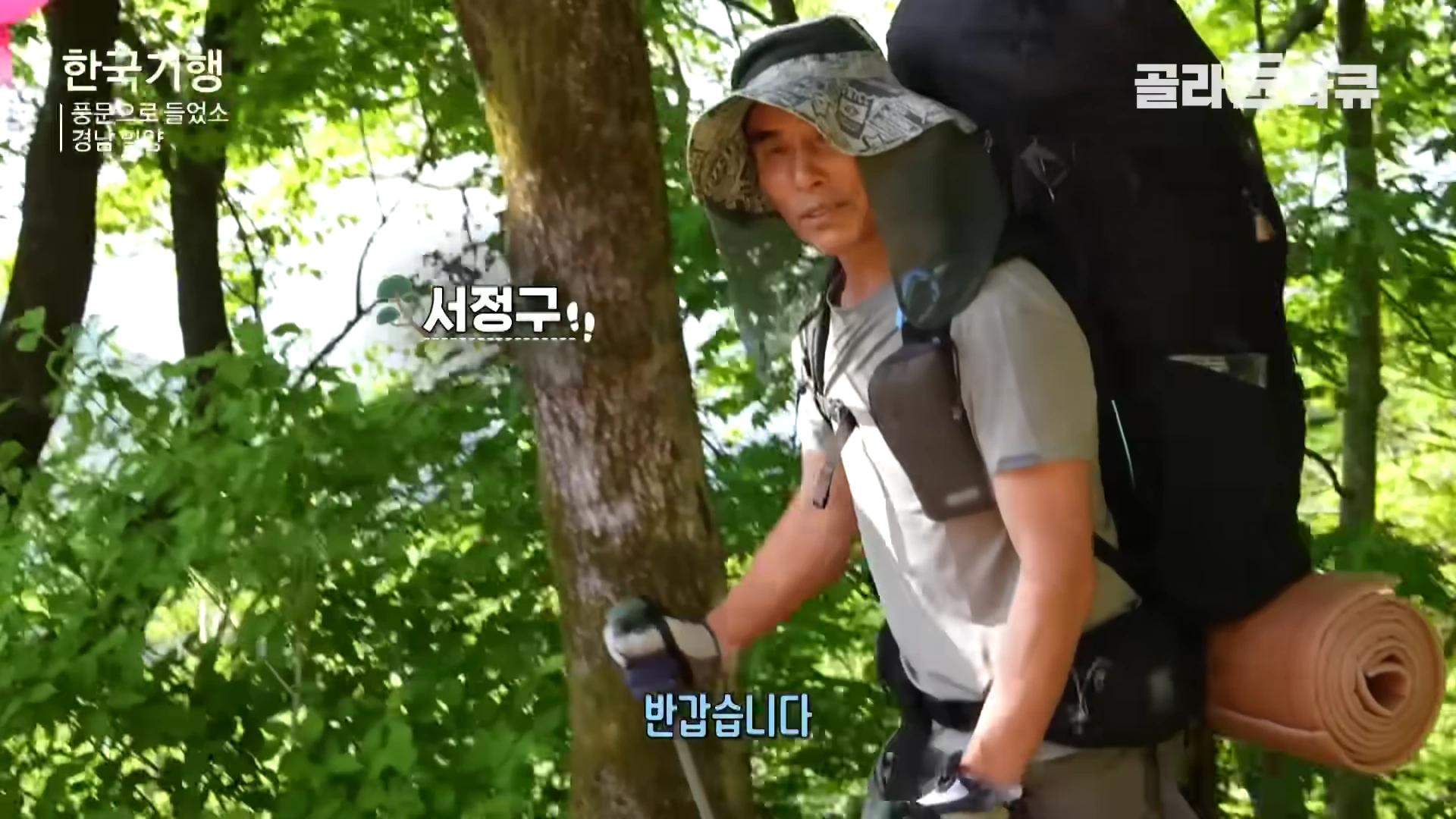 등산 모자를 쓴 남성이 커다란 배낭을 메고 숲길을 걷고 있다.