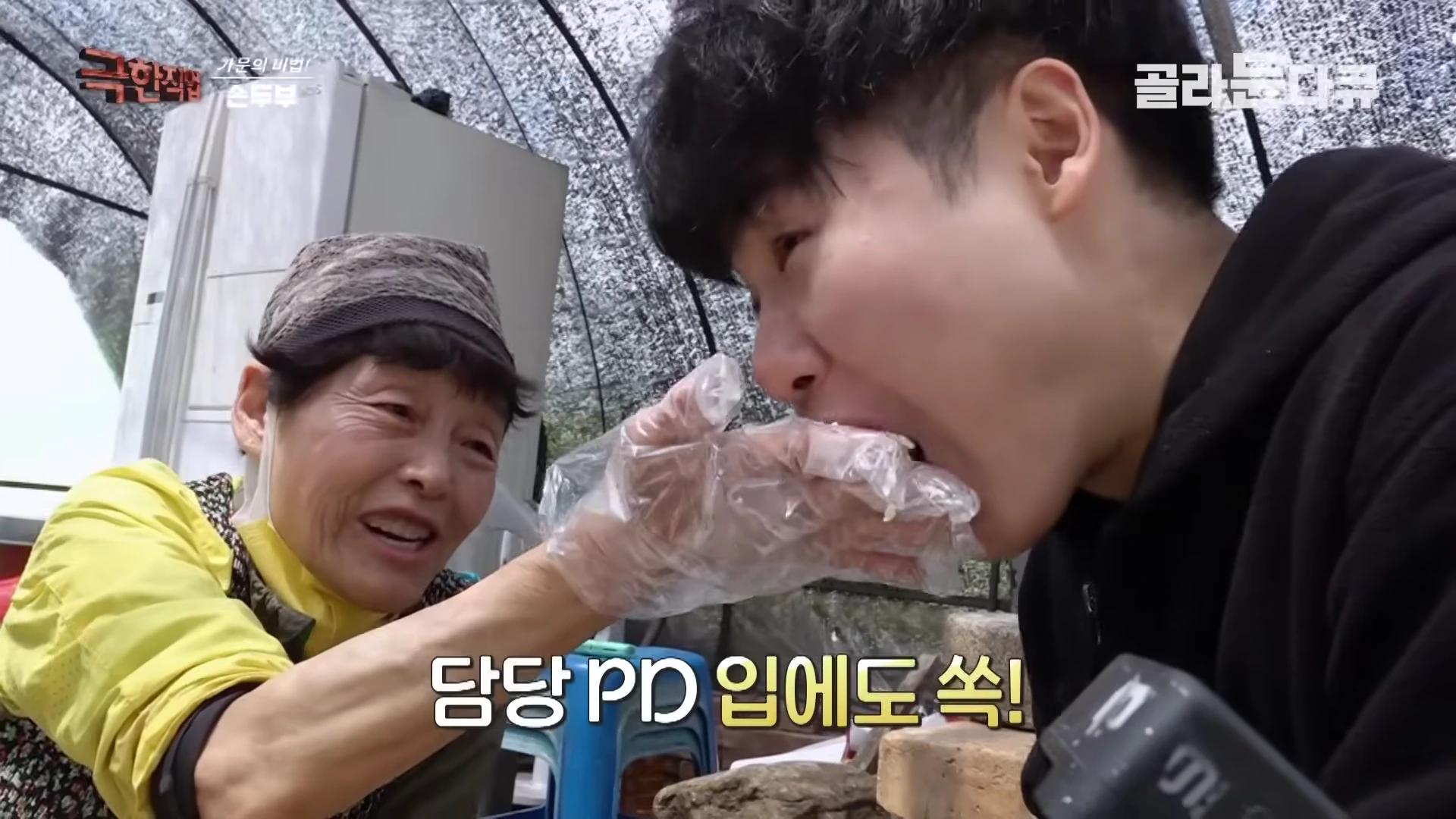 노란색 상의를 입은 할머니가 위생 장갑을 낀 손으로 젊은 남성에게 갓 만든 두부를 먹여주고 있다.