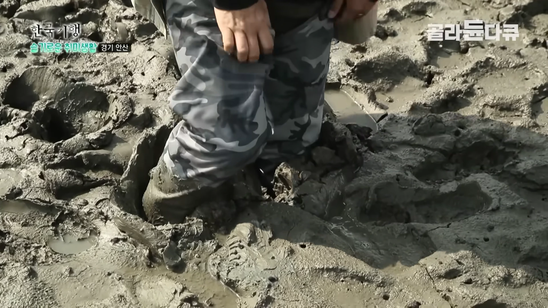 카무플라주 바지를 입은 사람이 발이 깊숙이 빠지는 진흙 갯벌 위에 서 있는 모습