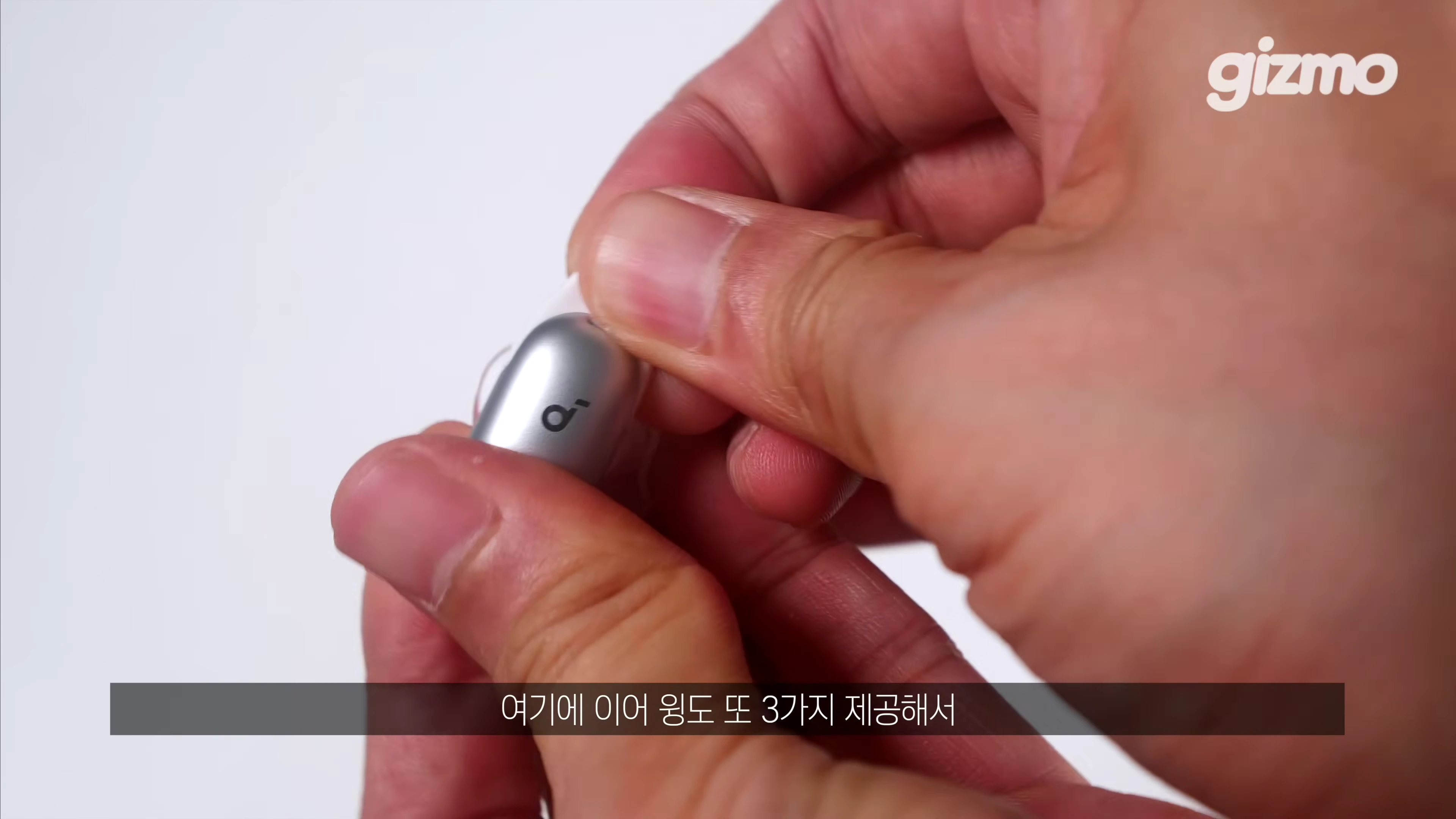 두 손으로 은색 무선 이어폰 본체의 이어팁 부분을 교체하거나 확인하고 있는 모습
