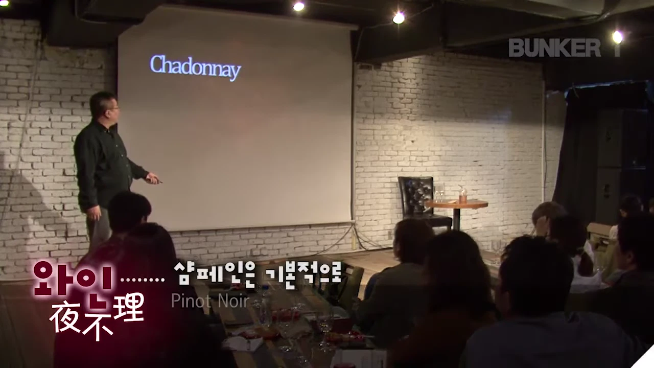 강단 위에서 발표자가 스크린에 띄워진 'Chardonnay'라는 글자를 가리키며 청중에게 설명하고 있는 강연 장면