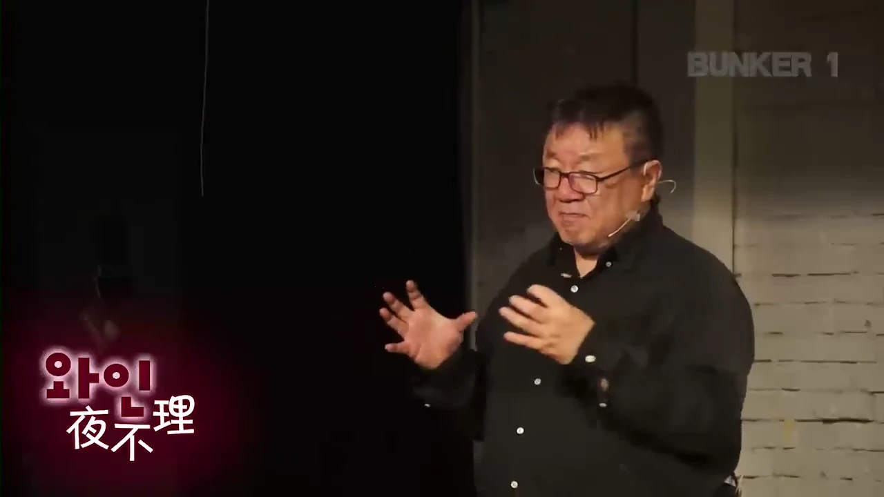 안경을 쓴 중년의 남성이 어두운 무대 위에서 손동작을 하며 강연을 하고 있는 모습