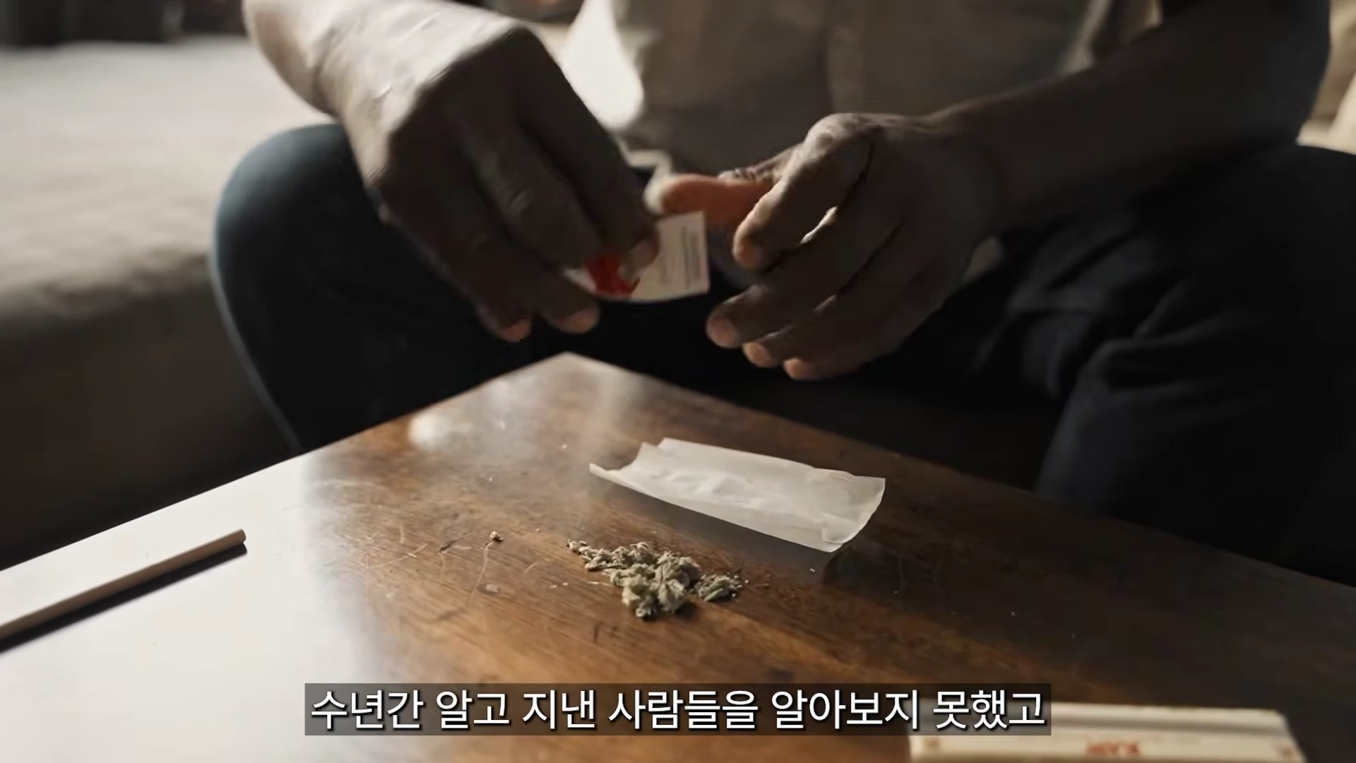 손으로 직접 담배를 만들기 위해 종이 위에 잎을 펴고 있는 사람의 모습이 담긴 클로즈업 영상 화면.