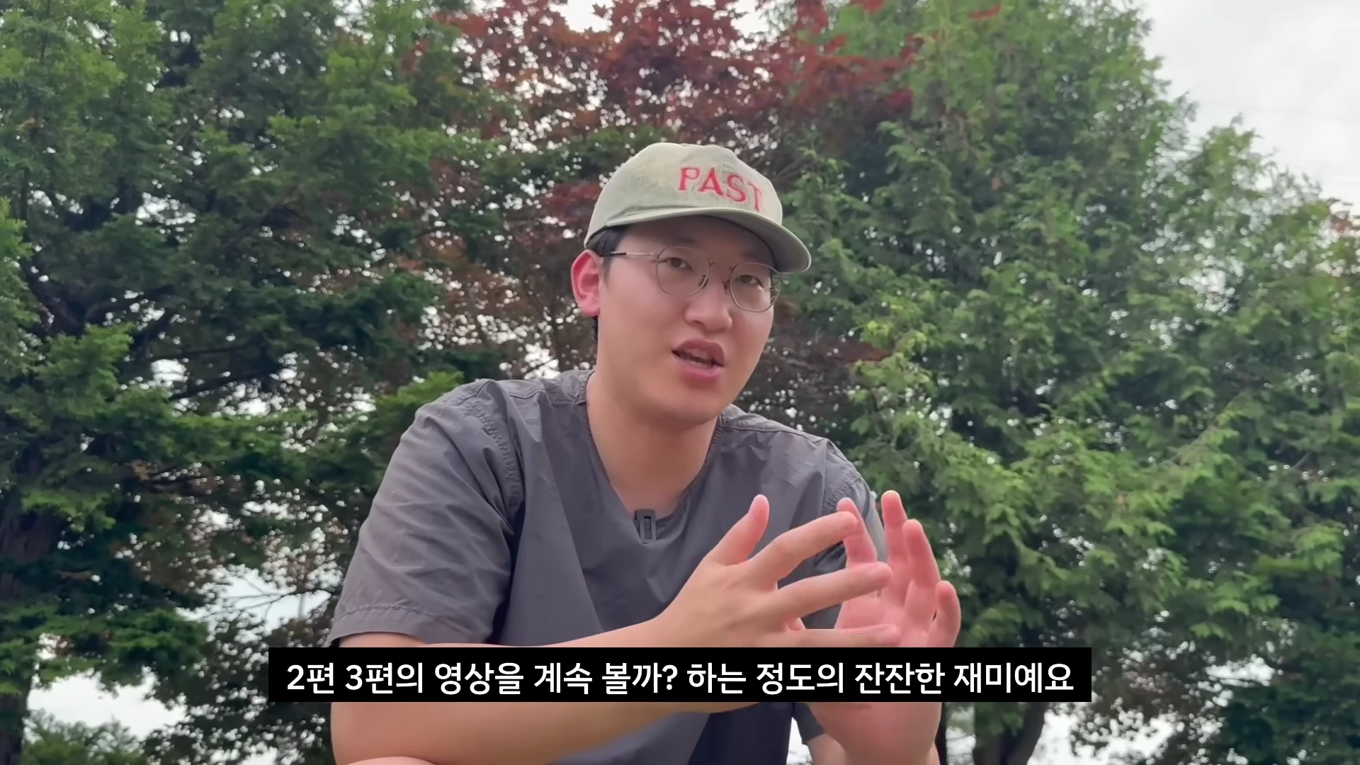 야외 정원을 배경으로 회색 셔츠를 입고 모자를 쓴 남성이 손짓을 하며 이야기를 하고 있고, 화면 하단에는 한국어 자막이 표시되어 있습니다.