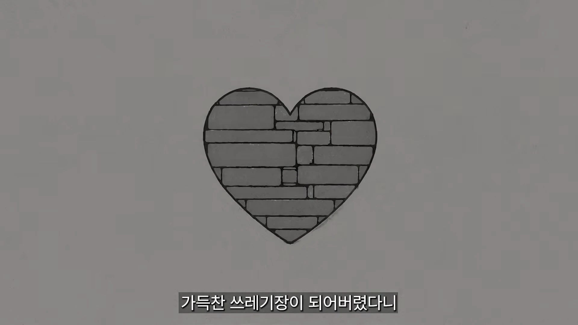 단색 배경 중앙에 돌담 패턴으로 채워진 하트 모양 그래픽이 그려져 있고, 그 아래에 흰색 자막으로 '가득찬 쓰레기장이 되어버렸다니'라는 문구가 쓰여 있습니다.