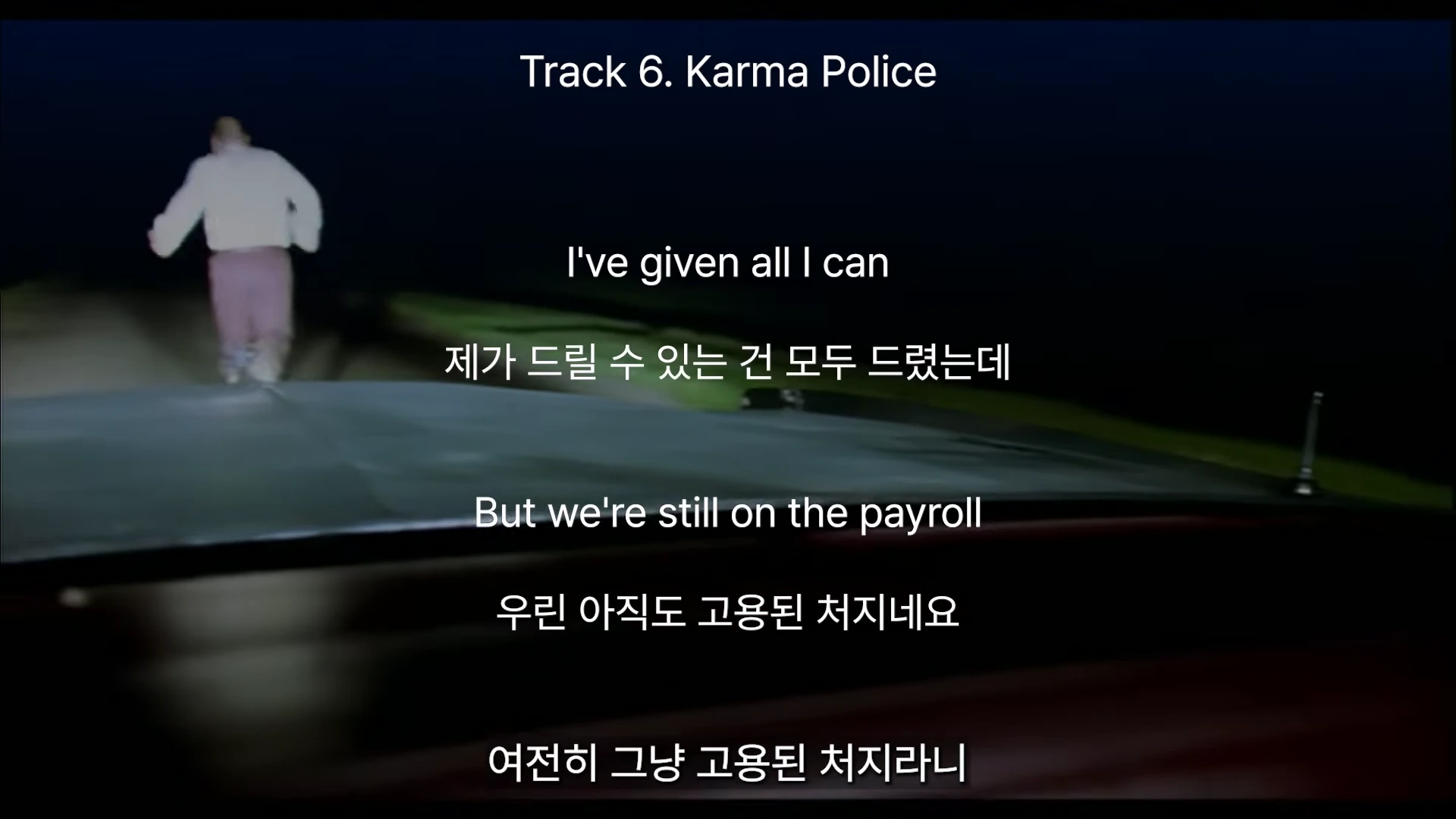 어두운 밤길을 달려가는 사람의 뒷모습이 차 내부에서 촬영된 화면 위에 트랙 제목과 영어 및 한국어 가사가 자막으로 표시되어 있다.
