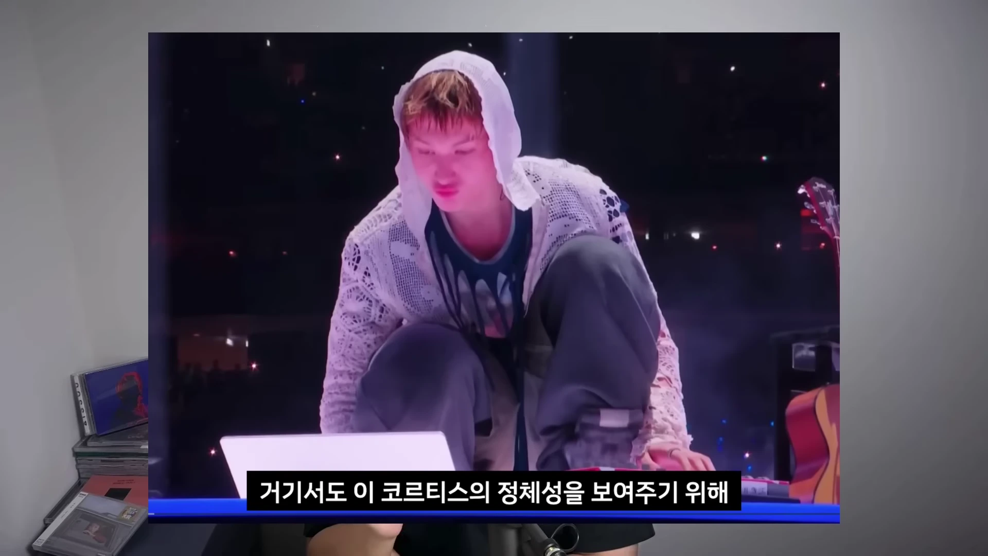 공연 무대 위에 후드티를 쓴 남성이 노트북을 앞에 두고 앉아 작곡 퍼포먼스를 하는 모습이 영상 프레임으로 보인다.