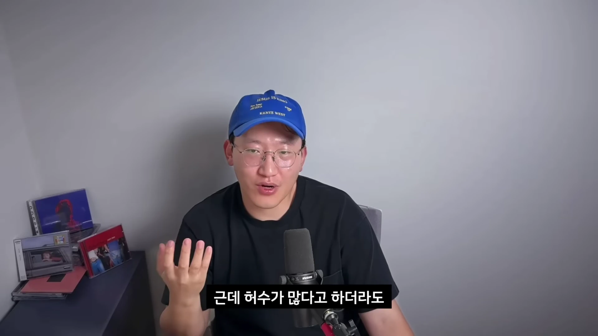 파란색 모자를 쓴 남성이 마이크 앞에서 손을 들어 설명하며 이야기하고 있는 영상 화면입니다.