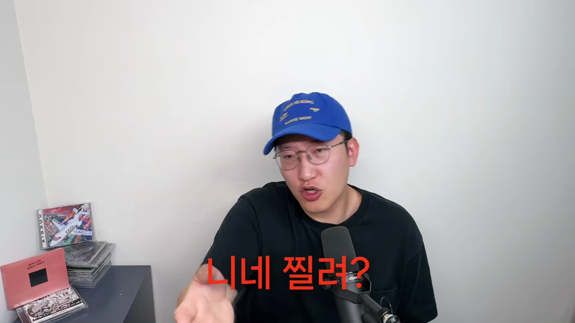 파란색 야구 모자를 쓰고 안경을 쓴 남성이 마이크 앞에 앉아 정면을 향해 질문을 던지고 있으며, 화면 중앙에는 빨간색 텍스트로 '니네 찔려?'라는 자막이 새겨져 있다.