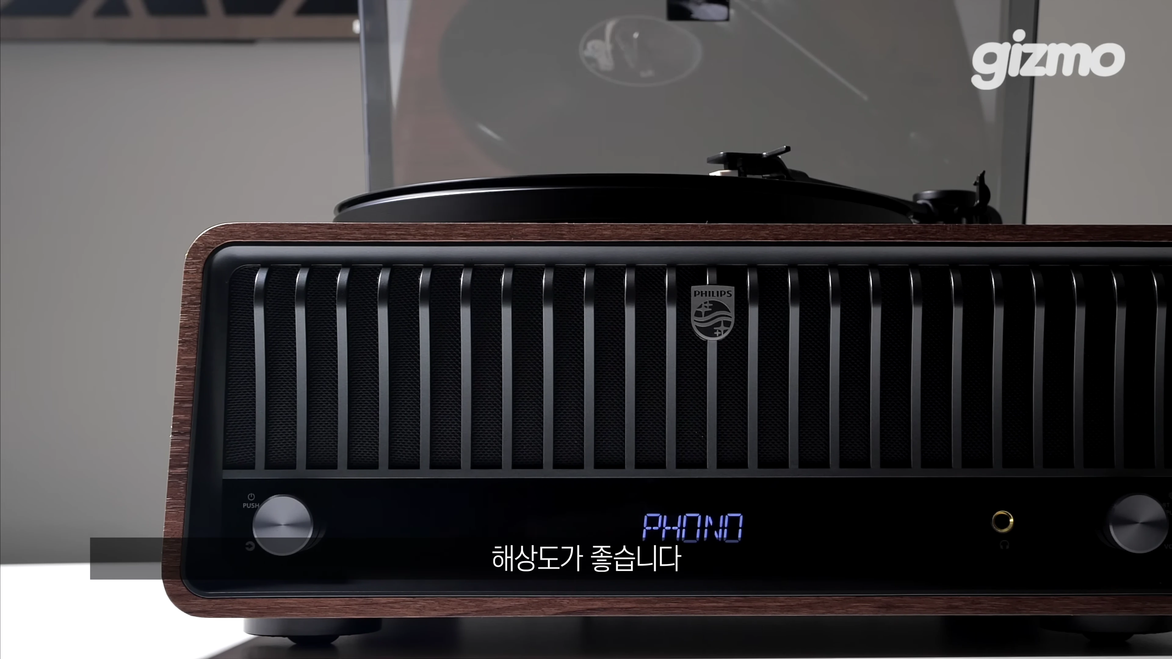 클래식한 디자인의 우드 프레임 필립스 일체형 턴테이블이 정면에서 보이며, 전면에 PHONO라는 문구가 표시된 검은색 스피커 그릴과 컨트롤 노브가 배치되어 있습니다.