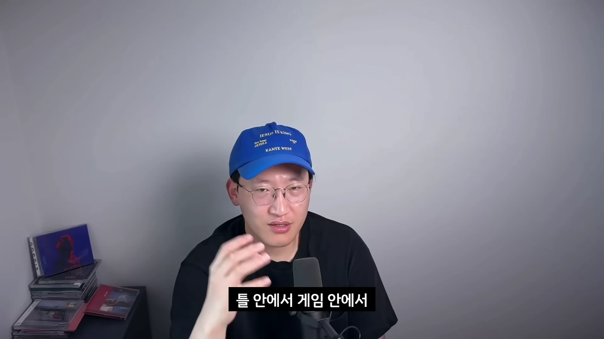 파란색 야구 모자를 쓴 안경을 낀 남성이 앞에 있는 마이크를 향해 손짓하며 이야기하고 있다.