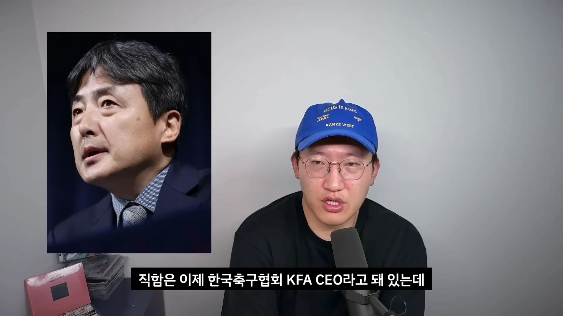 파란색 모자를 쓴 남성이 마이크 앞에서 이야기하고 있고, 화면 왼쪽에는 정장 차림의 남성 사진이 수직으로 삽입되어 있습니다.
