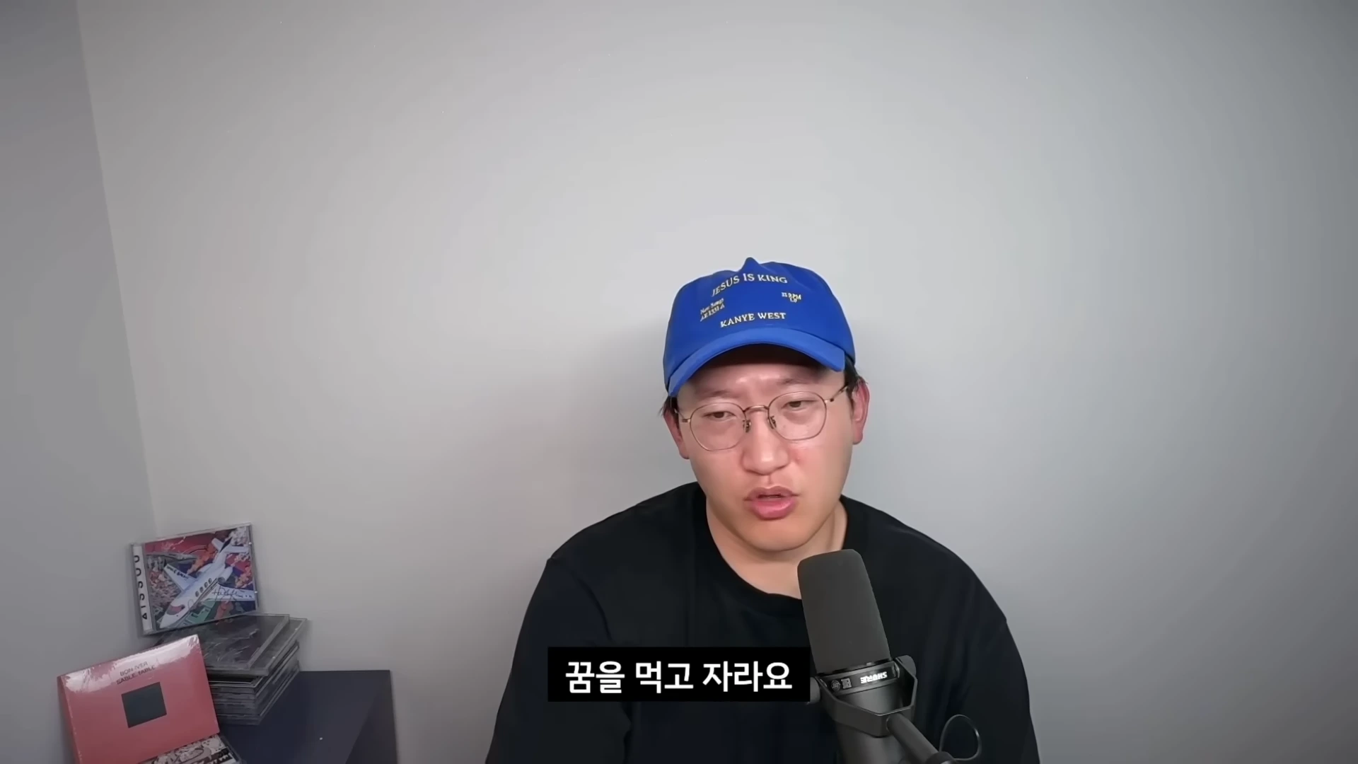 파란색 야구 모자와 안경을 쓴 남성이 마이크 앞에서 이야기하고 있는 모습
