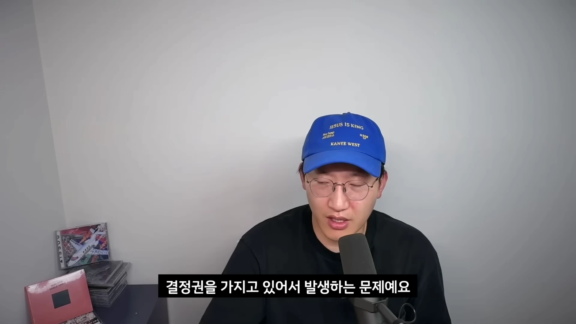 파란색 야구 모자와 안경을 쓴 남성이 마이크 앞에서 이야기를 하고 있는 모습입니다.