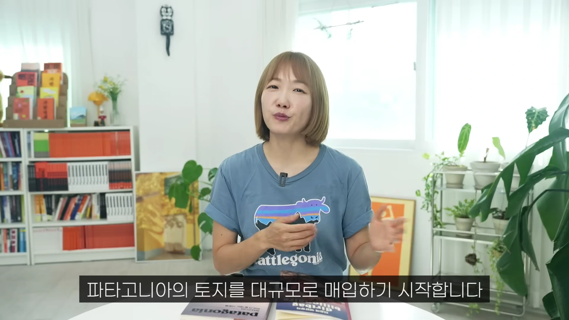 밝은 실내를 배경으로 단발머리의 여성이 파란색 티셔츠를 입고 이야기를 하고 있으며, 화면 하단에는 '파타고니아의 토지를 대규모로 매입하기 시작합니다'라는 자막이 보입니다.