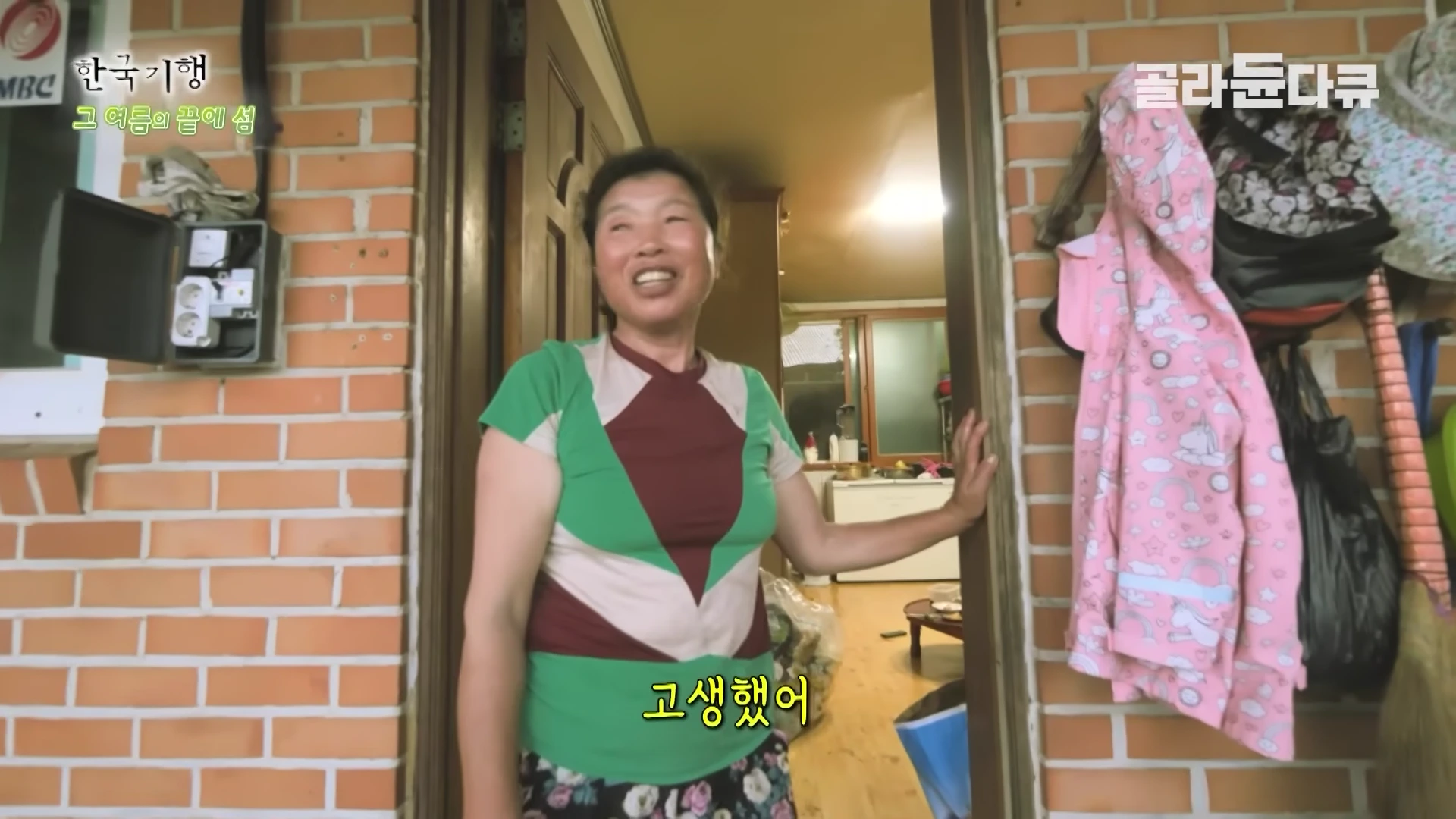 붉은 벽돌집 문 앞에 서서 환하게 웃고 있는 중년 여성의 모습이 담긴 방송 화면