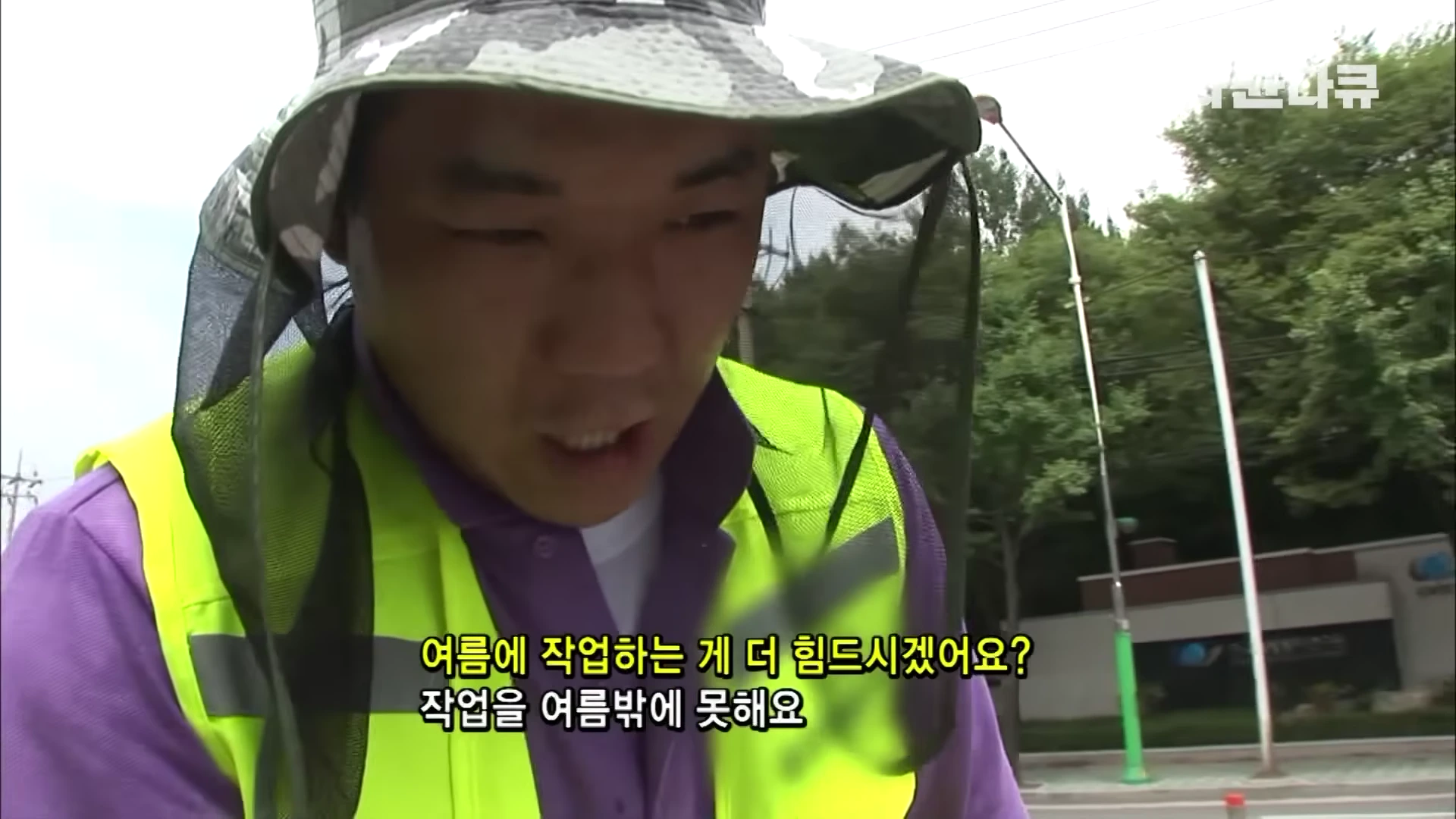 얼굴을 가리는 망사가 달린 모자를 쓴 작업자가 인터뷰하고 있으며 화면 중앙에는 질문과 대답이 자막으로 표시되어 있다.