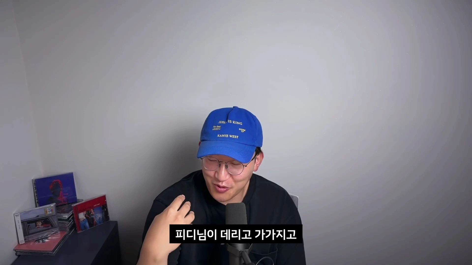 파란색 모자를 쓰고 안경을 쓴 남성이 마이크 앞에서 이야기하고 있다.