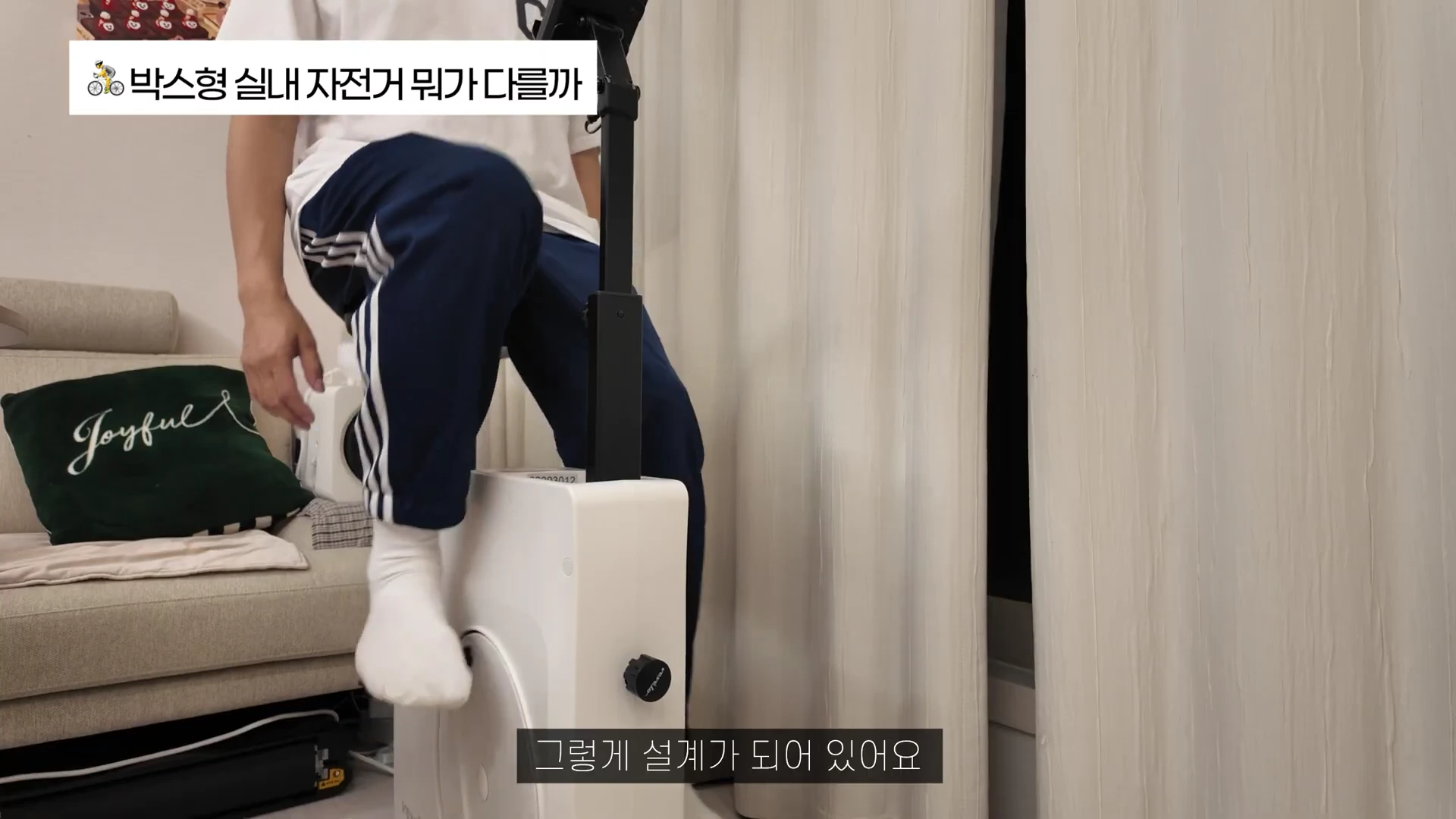 실내 안장에서 자전거를 타는 사람의 다리 모습과 함께 박스형 디자인의 실내자전거 프레임이 보여지며 상단에는 관련 문구가 박힌 영상 캡처 화면.