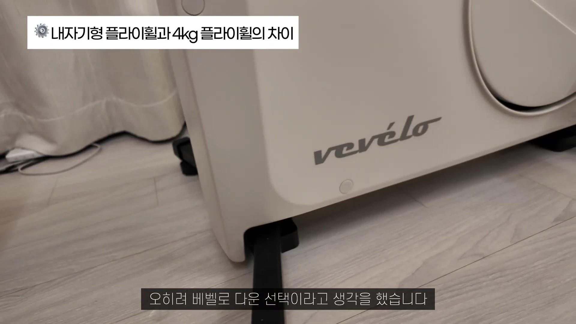 실내자전거의 하단부를 근접 촬영한 영상으로, 크림색 본체에 베벨로 로고가 적혀 있고 위쪽에는 내자기형 플라이휠과 4kg 플라이휠의 차이라는 자막이 떠 있습니다.