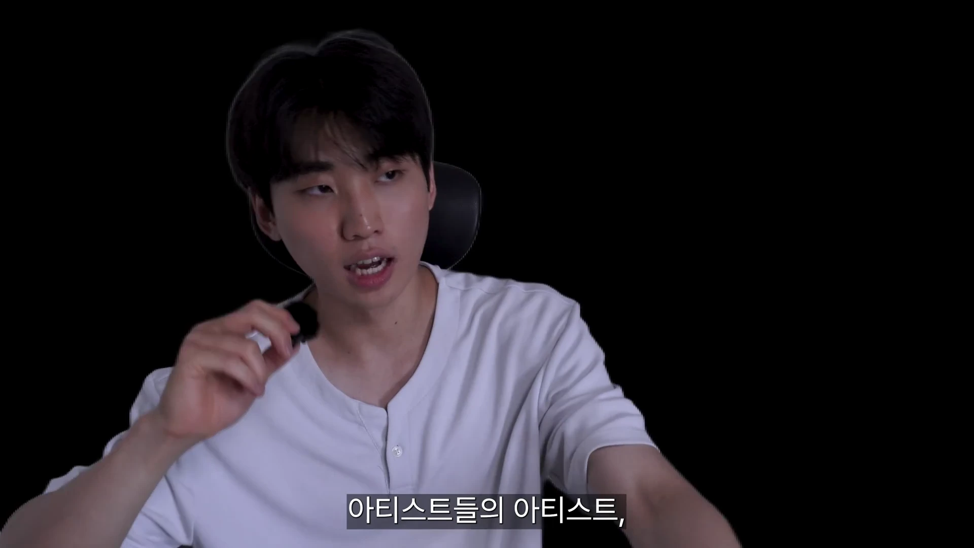흰색 티셔츠를 입은 남성이 검은 배경 앞에서 마이크를 잡고 이야기를 나누고 있다.