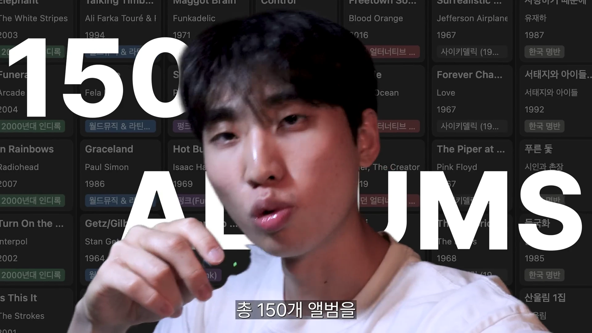 화면 중앙에 젊은 남성이 서 있고, 배경에는 앨범 제목과 연도가 쓰인 그리드 형태의 차트가 배치되어 있으며, 그 위에 '150 ALBUMS'라는 큰 흰색 글자가 합성되어 있다.