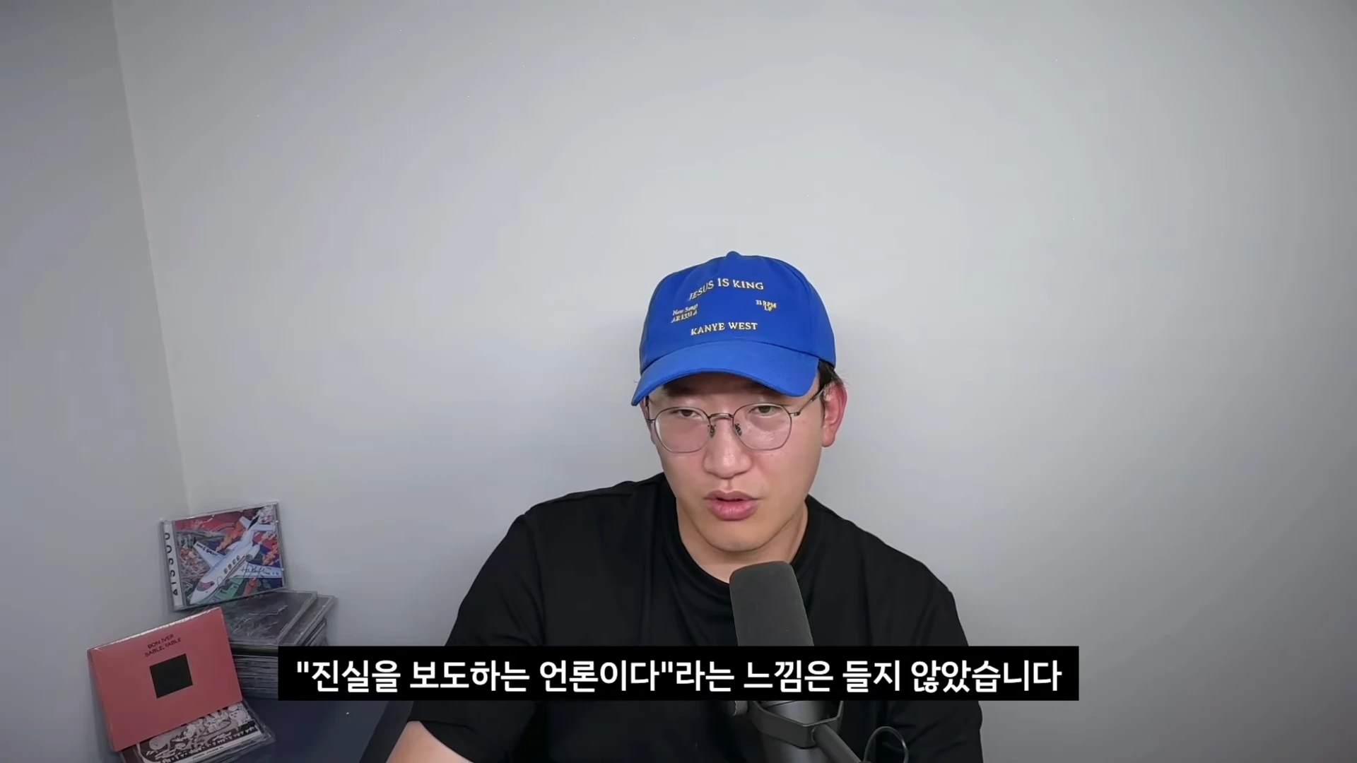파란색 야구 모자를 쓴 남성이 마이크 앞에서 진지한 표정으로 이야기하고 있으며, 화면 하단에는 자막이 쓰여 있다.