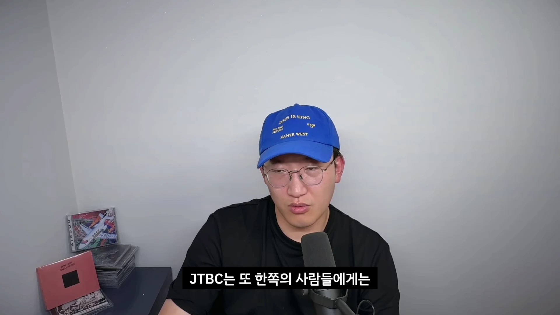파란색 야구 모자를 쓰고 안경을 쓴 남성이 마이크 앞에 앉아 이야기를 하고 있으며, 하단에 JTBC에 대한 자막이 흐릅니다.