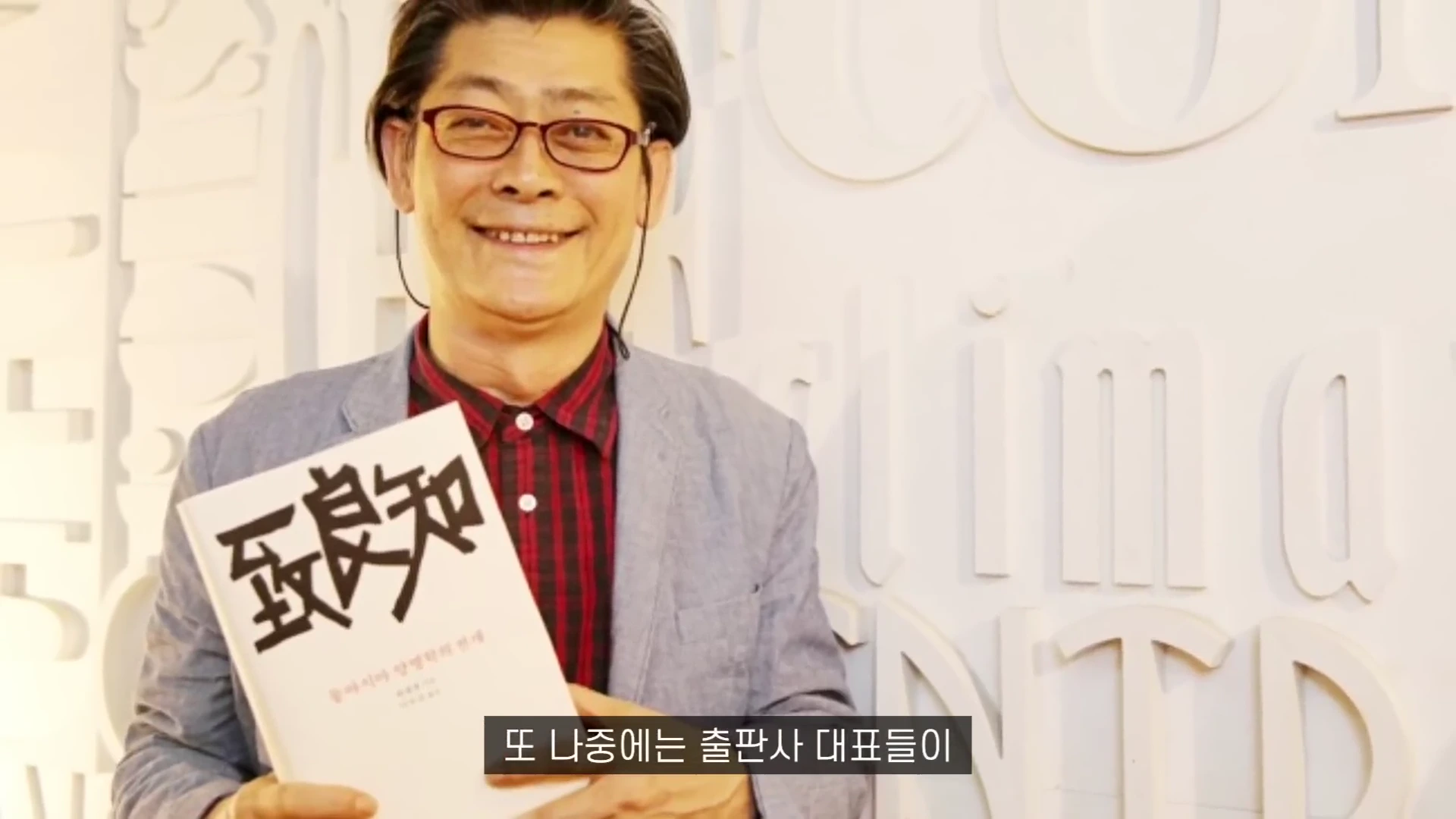 흰색 책을 손에 들고 환하게 웃고 있는 안경 쓴 중년 남성