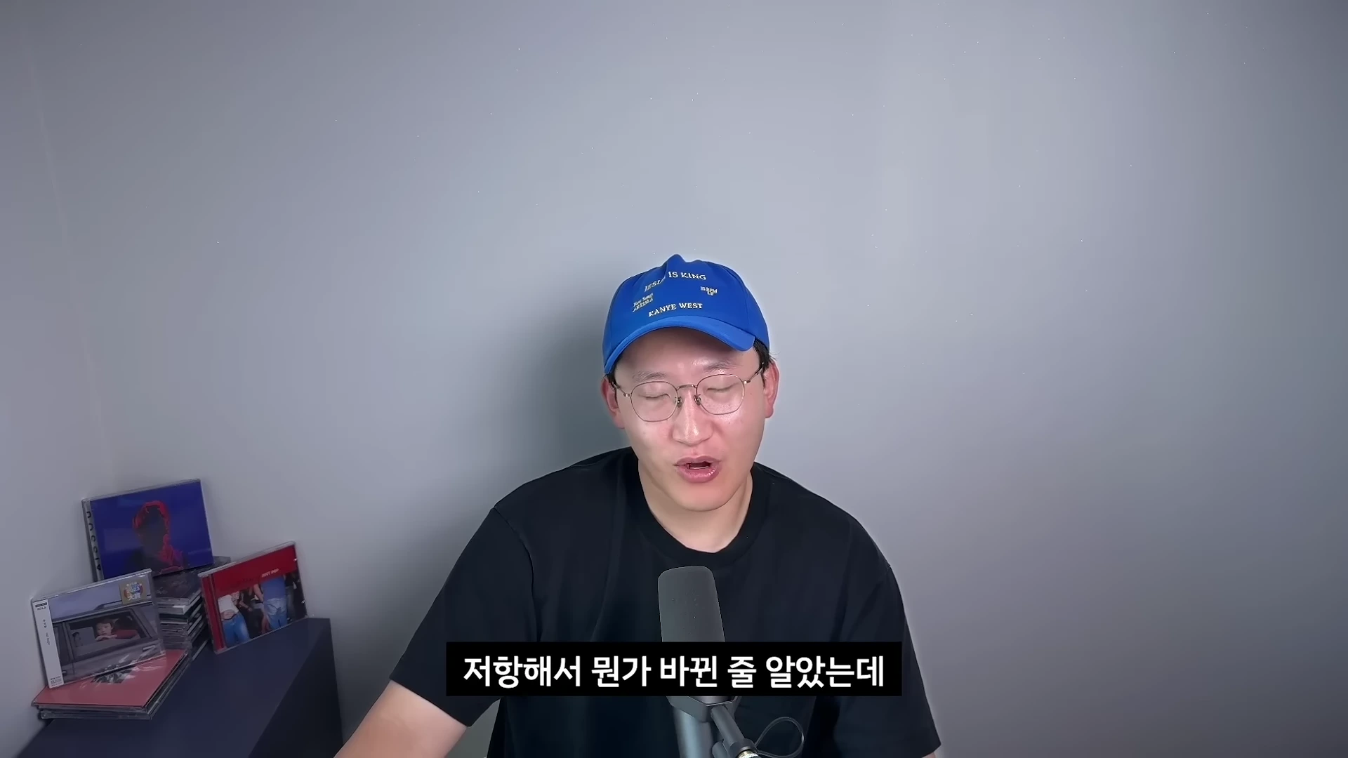 파란색 야구 모자와 안경을 쓴 남성이 마이크 앞에 앉아 이야기를 나누고 있는 모습이다.