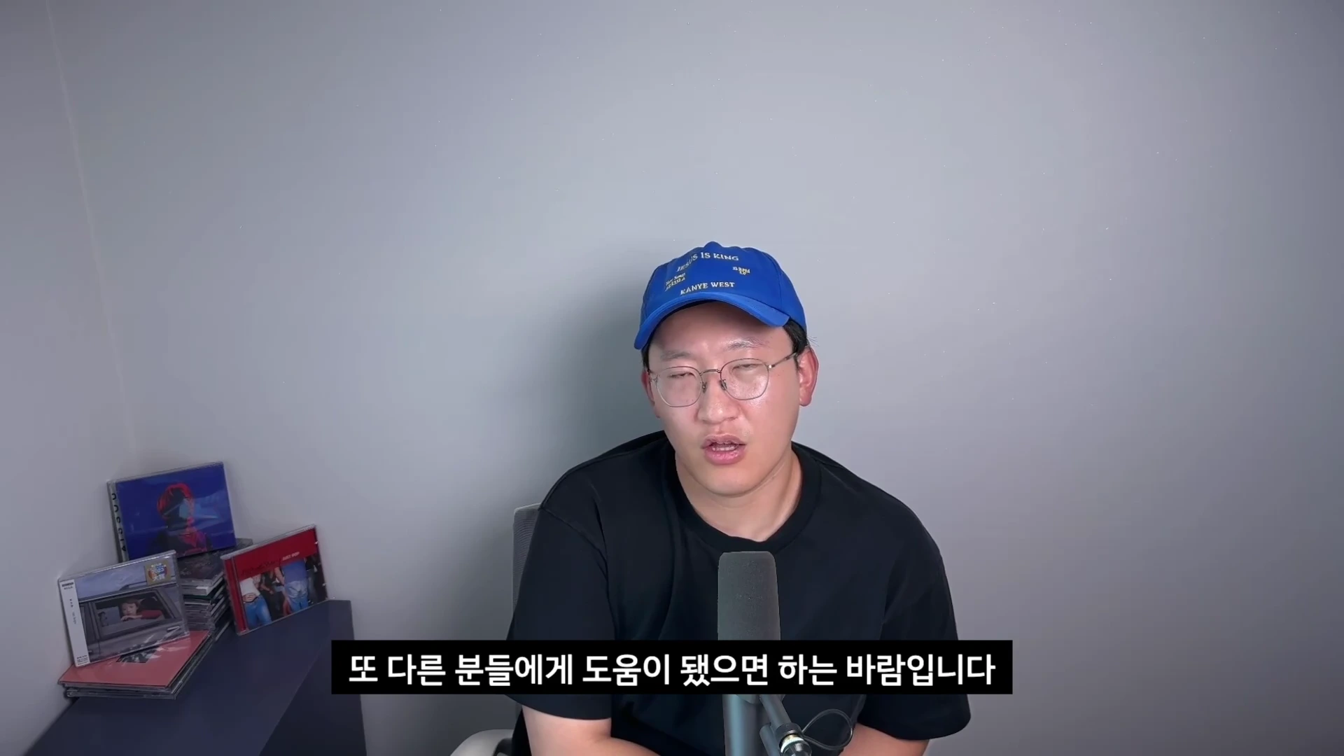 파란색 야구 모자와 안경을 쓴 남성이 마이크 앞에서 이야기하고 있으며 하단에는 한국어 자막이 표시되어 있다.